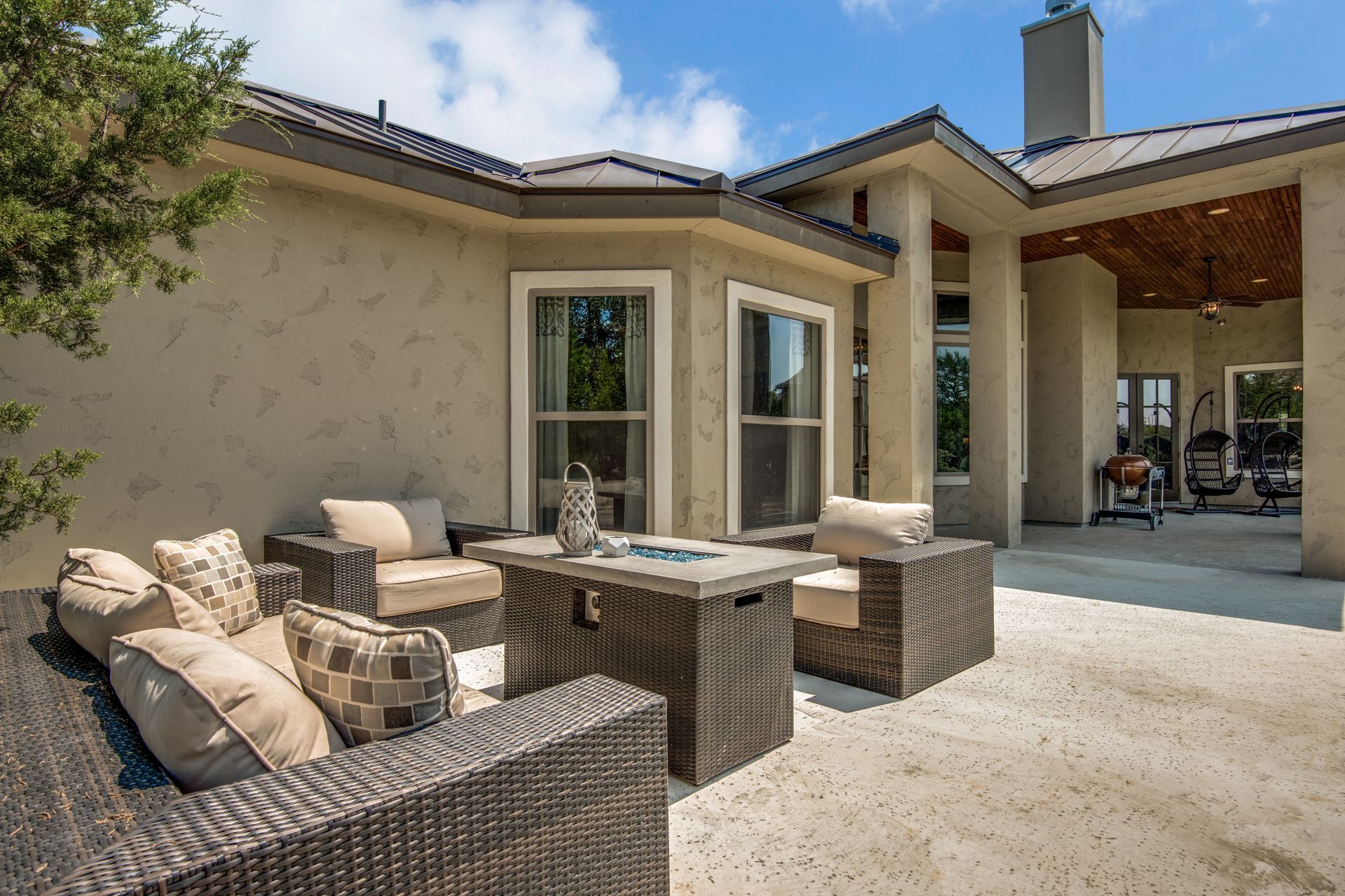 A patio with wicker furniture and a fire pit in front of a house.