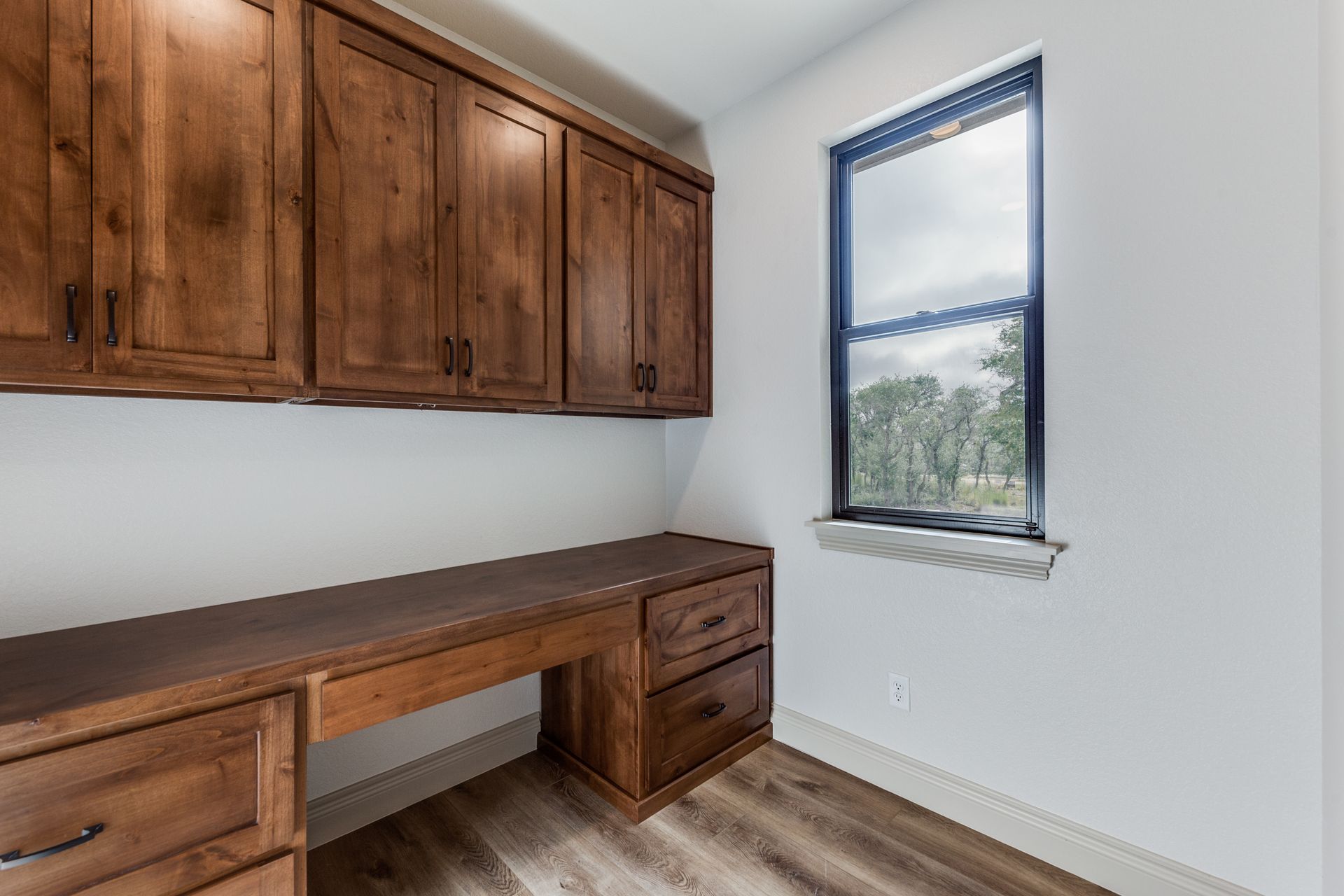 A room with a desk , cabinets , drawers and a window.