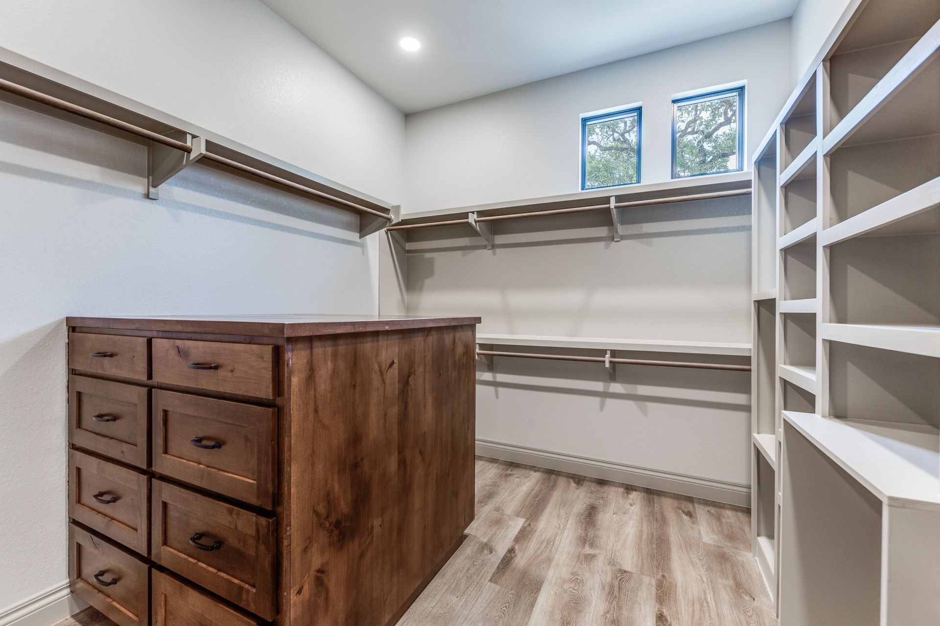 A walk in closet with a wooden dresser and shelves.