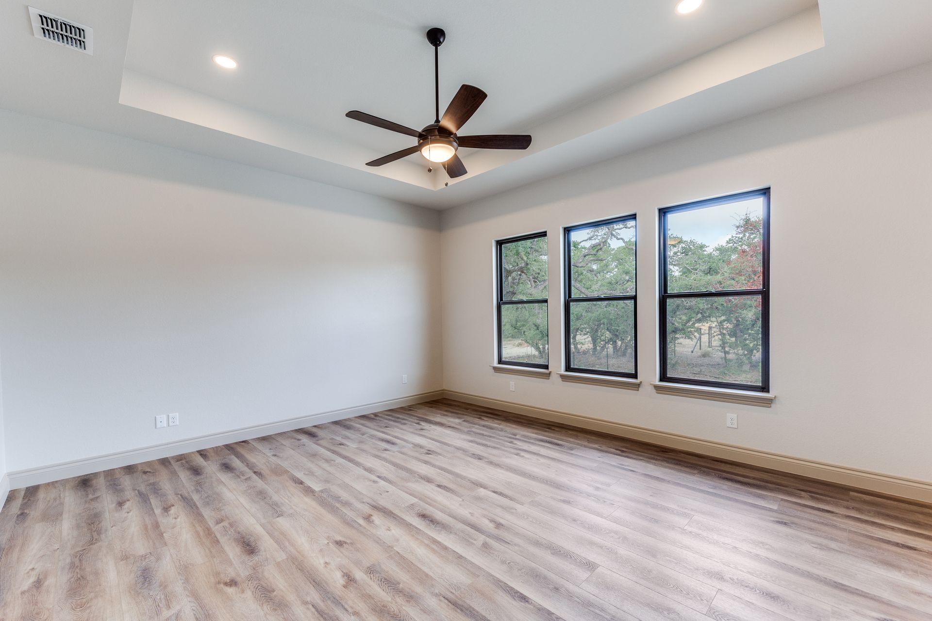 An empty bedroom with hardwood floors and a ceiling fan.