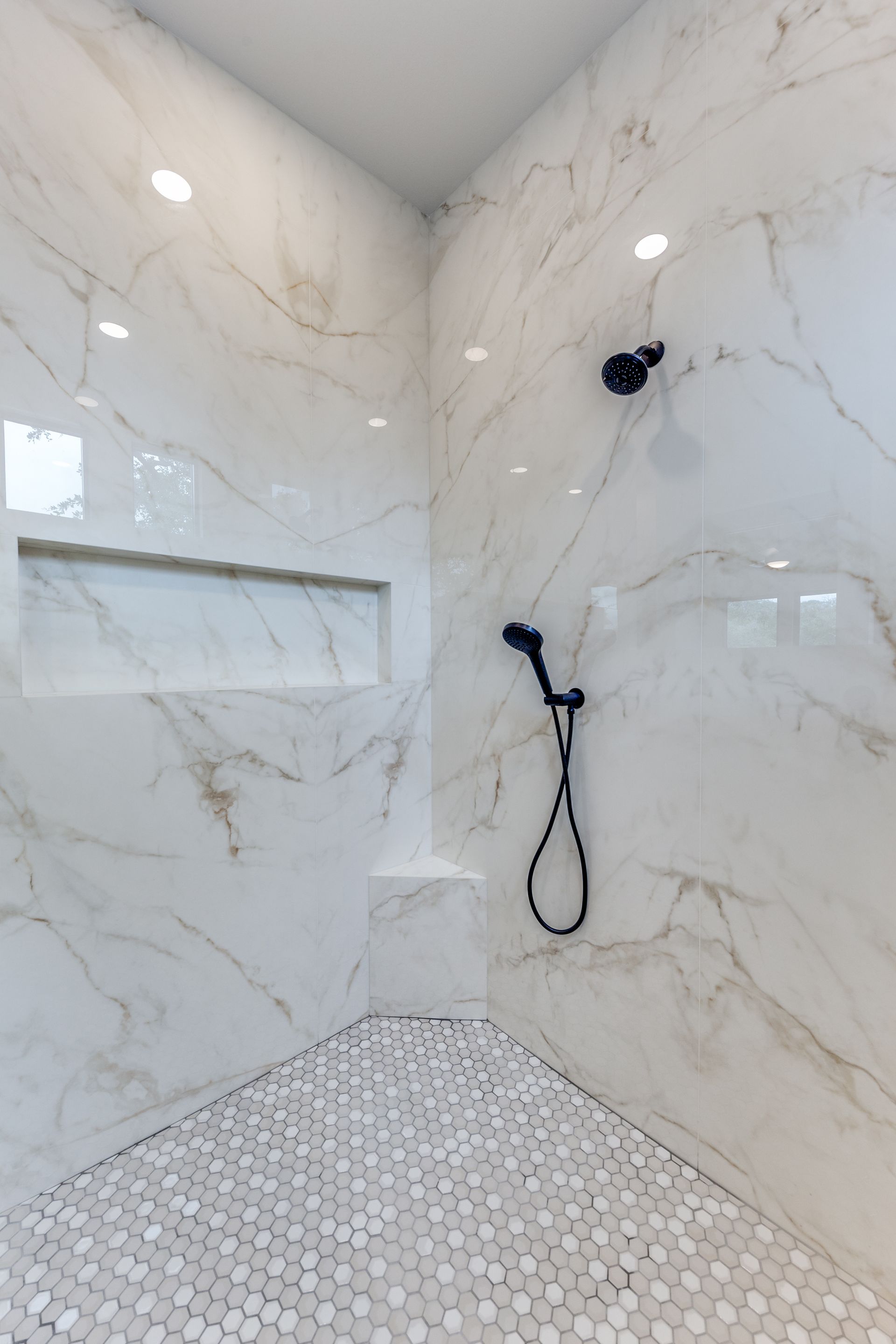 A shower with marble walls and a black shower head.
