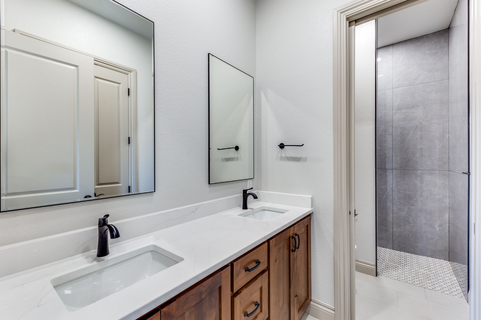A bathroom with two sinks , two mirrors and a walk in shower.