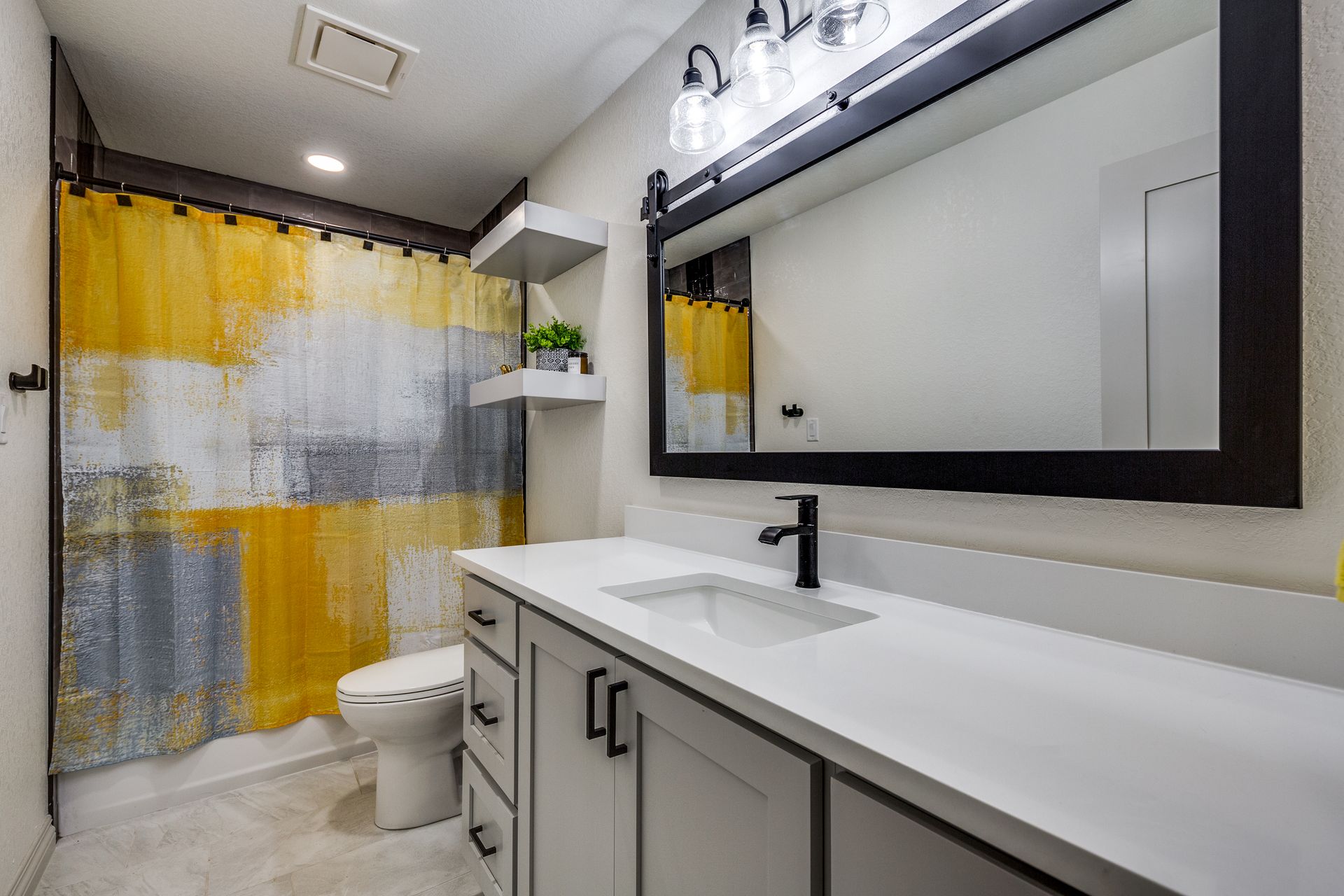 A bathroom with a toilet , sink , mirror and shower curtain.