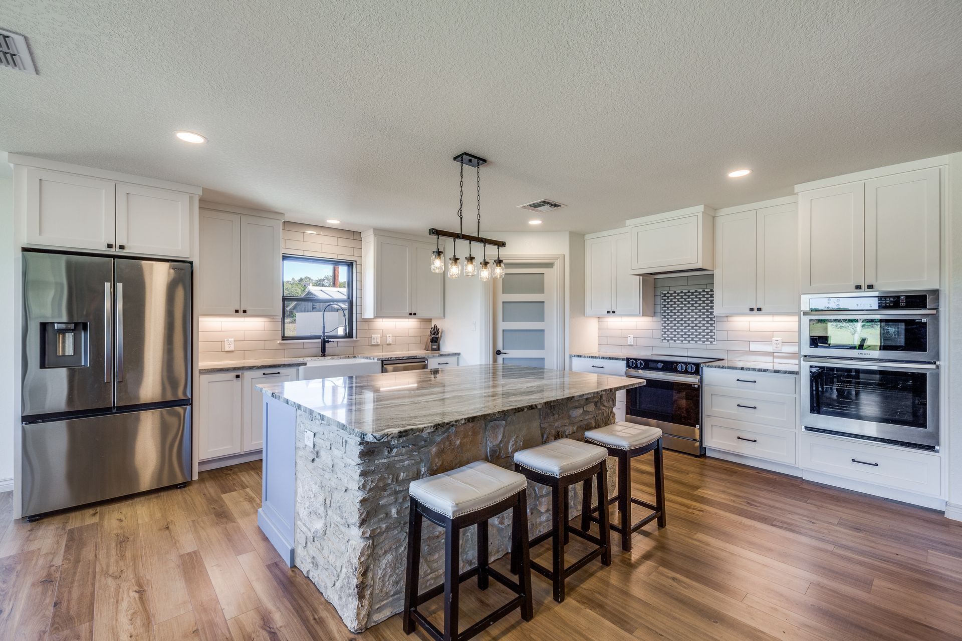 A kitchen with white cabinets , stainless steel appliances , a large island and stools.