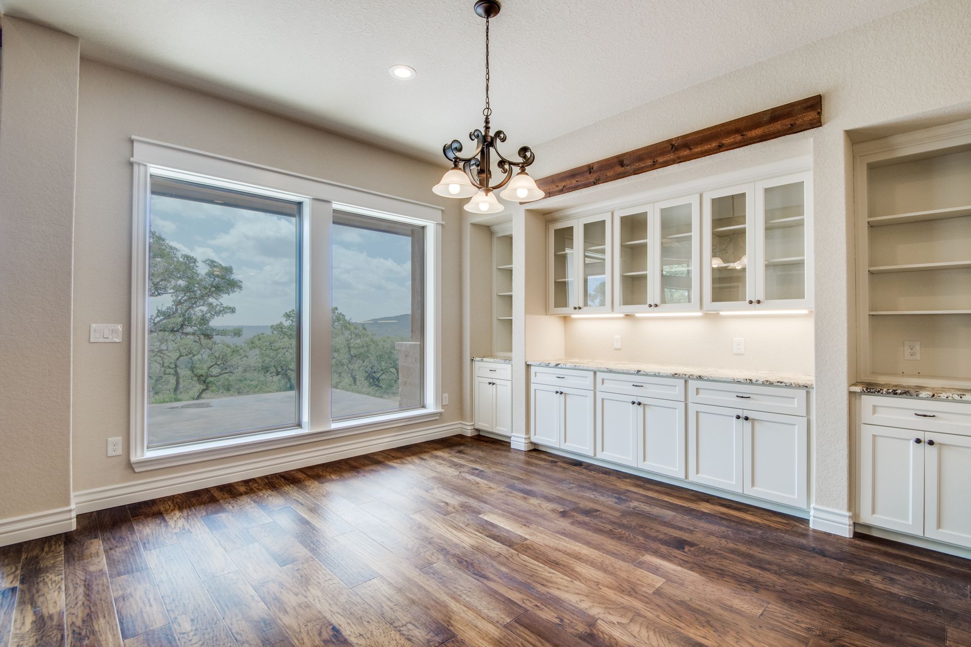 An empty room with hardwood floors , white cabinets , and a chandelier.
