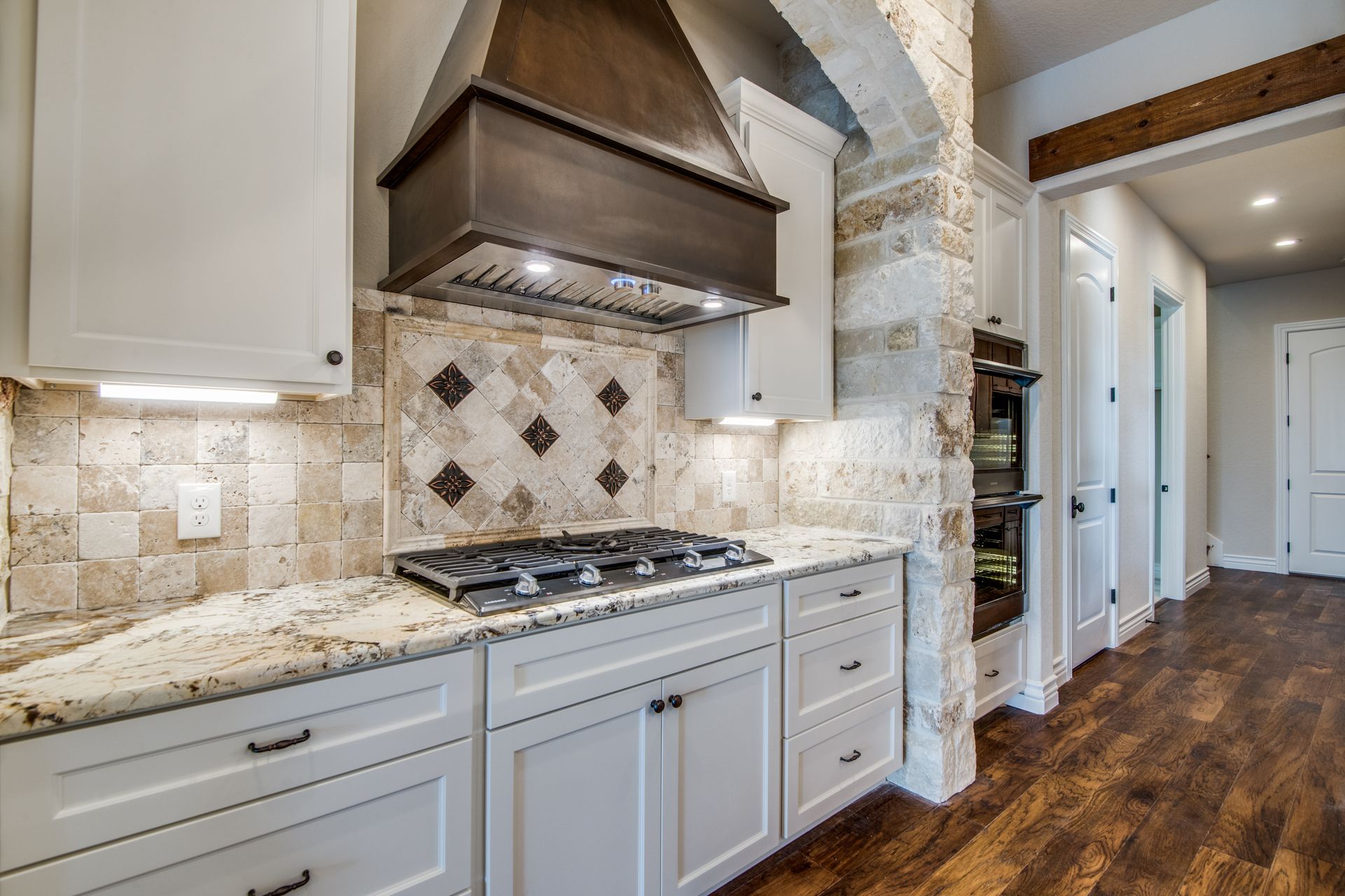 A kitchen with white cabinets , granite counter tops , a stove and a hood.