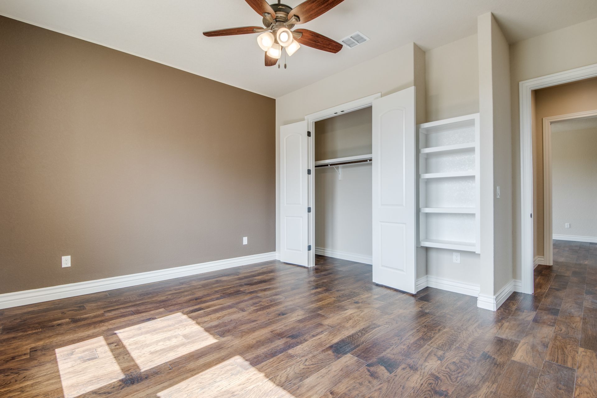An empty bedroom with hardwood floors and a ceiling fan.