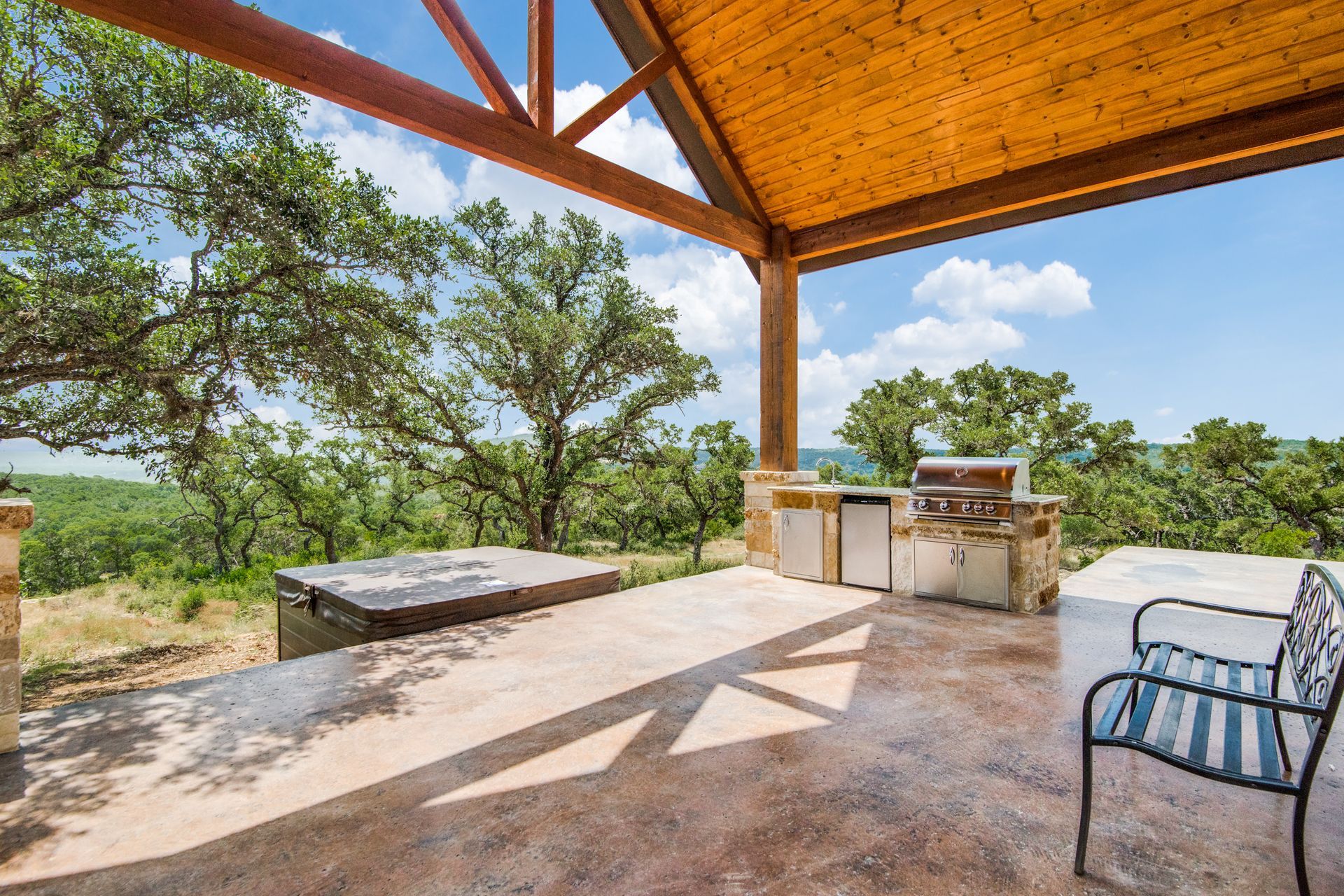 A patio with a grill and a bench under a wooden roof.