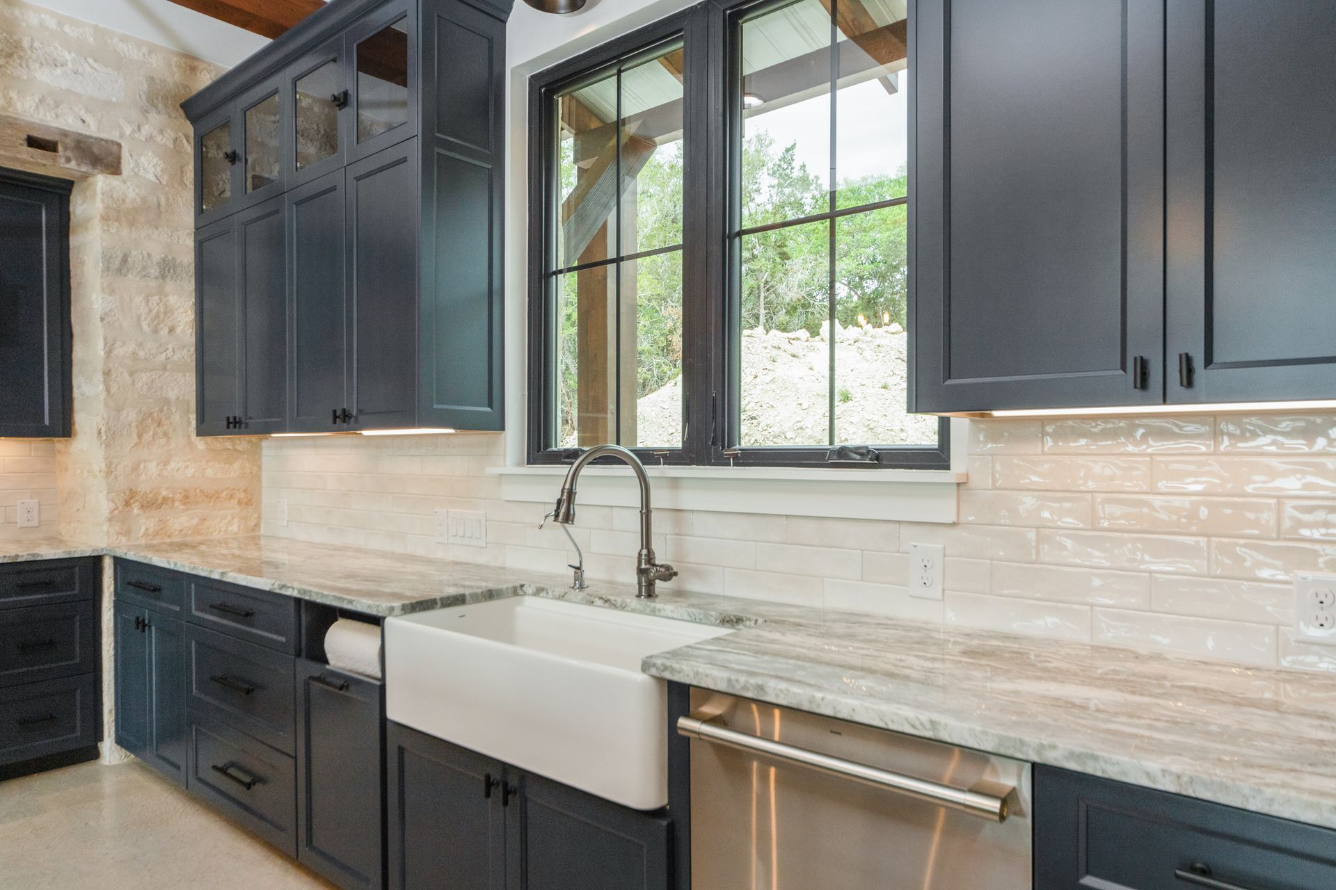 A kitchen with black cabinets , granite counter tops , stainless steel appliances and a farmhouse sink.