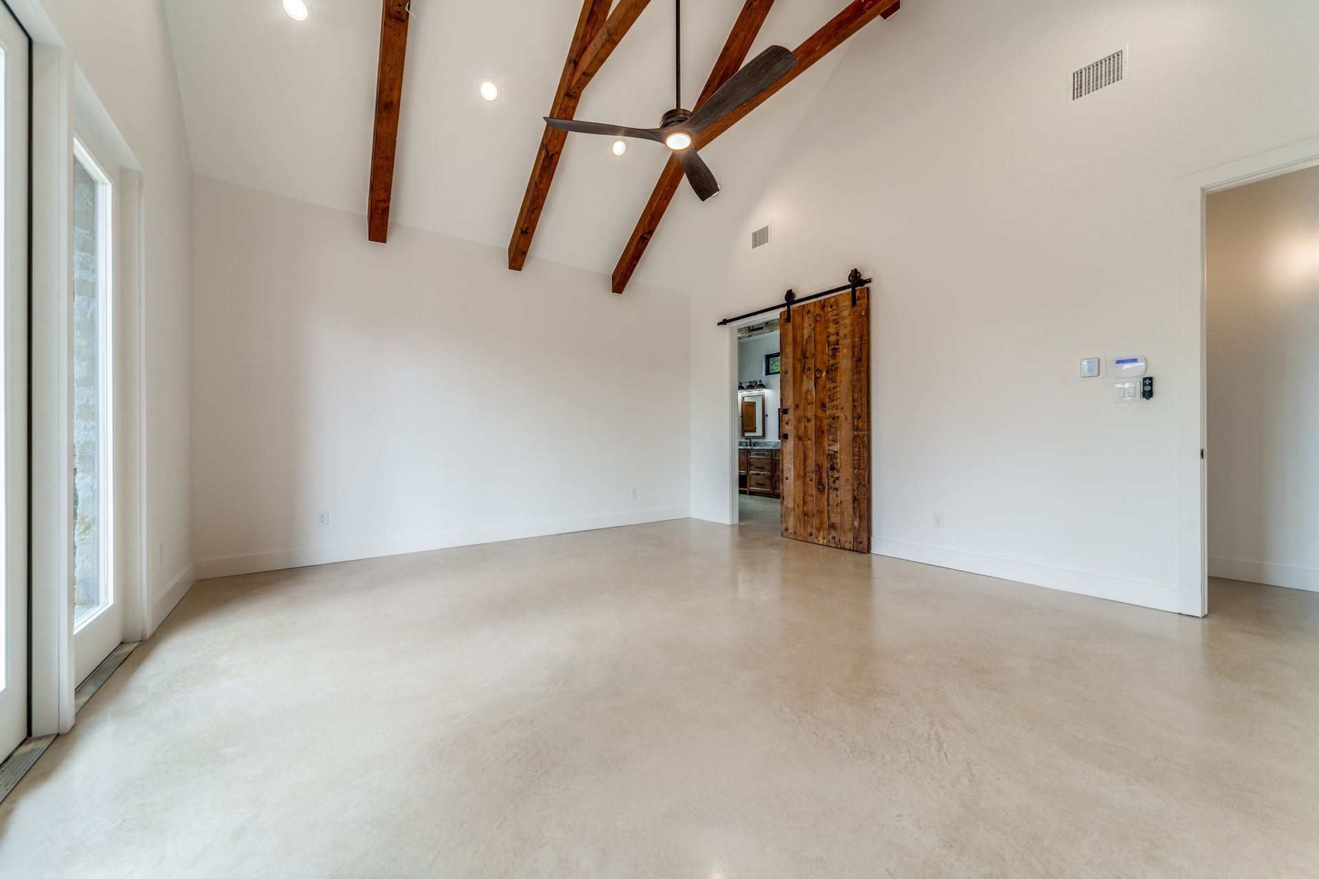 A large empty room with a ceiling fan and a sliding barn door.