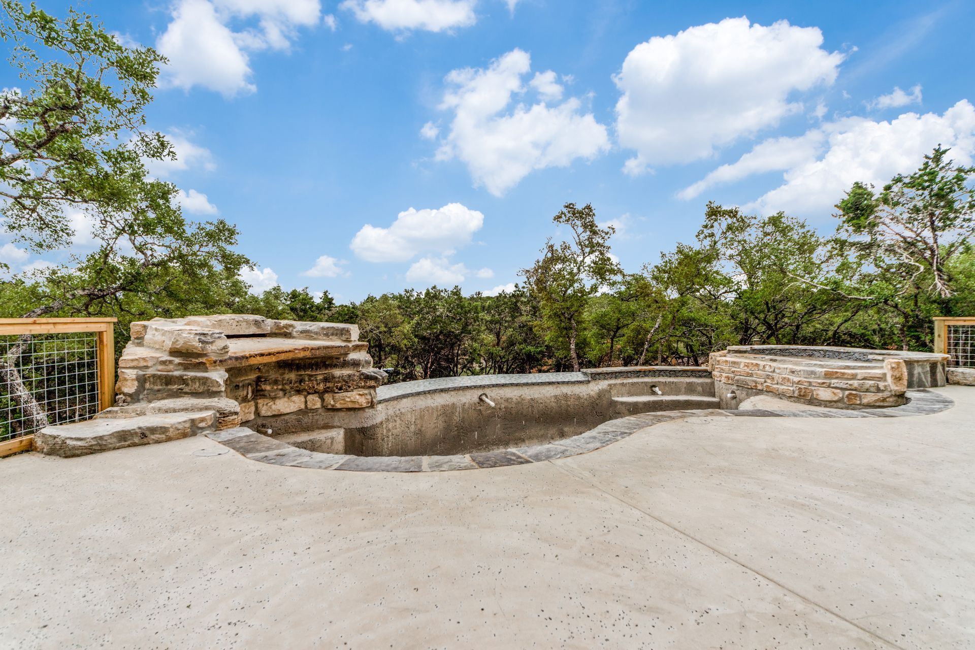 A large swimming pool is surrounded by trees and a fence.