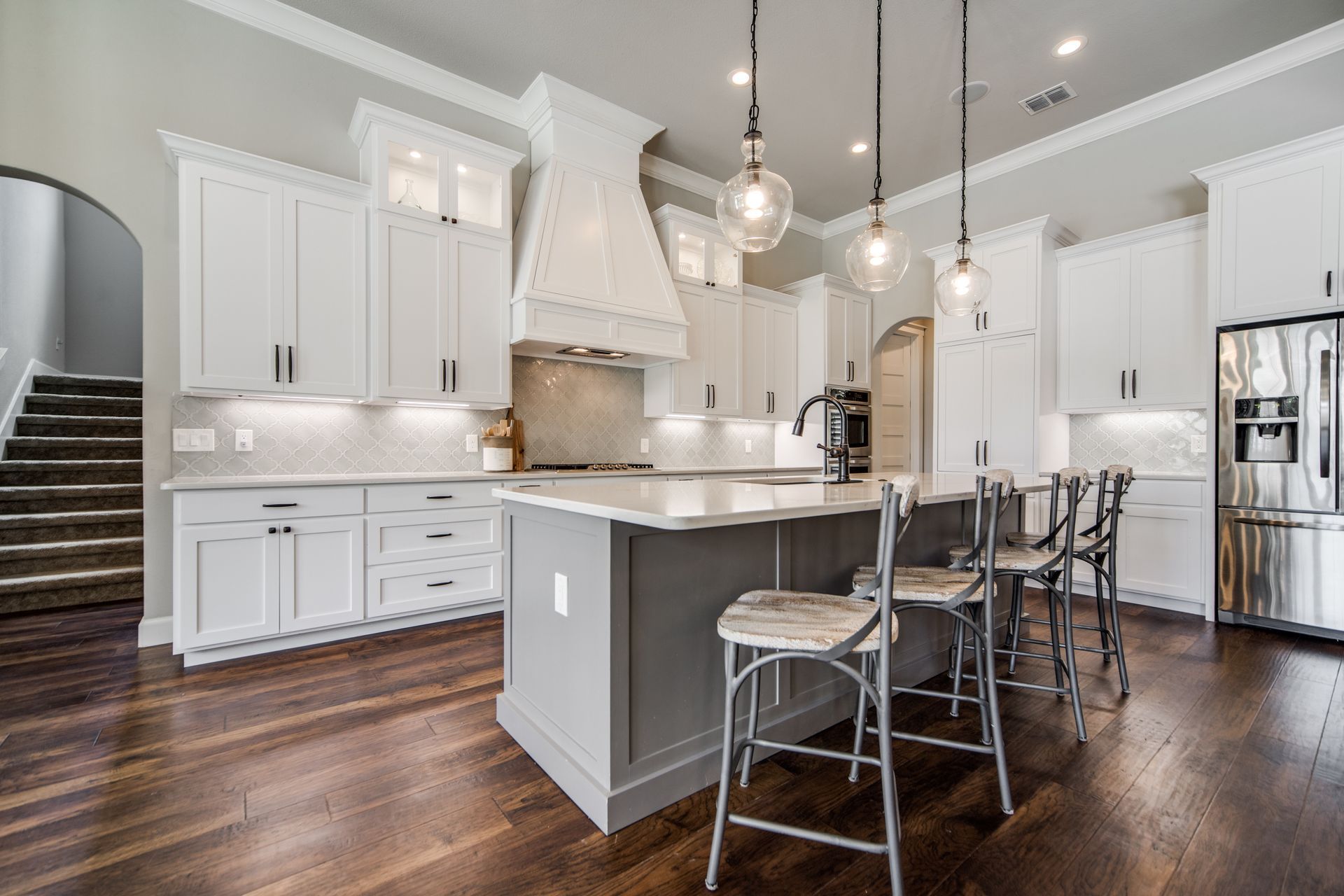 A kitchen with white cabinets , stainless steel appliances , hardwood floors and a large island.