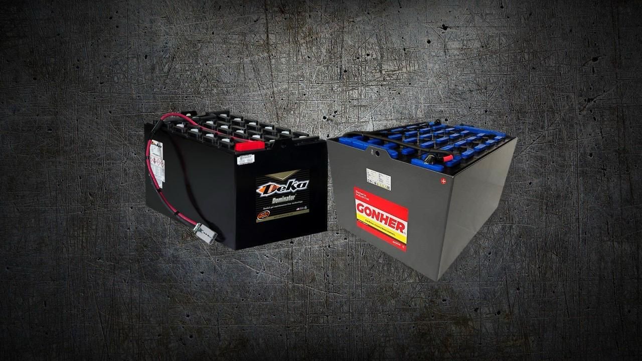 Dos baterías industriales, una negra y otra gris, se encuentran una al lado de la otra sobre un fondo gris oscuro y texturizado.