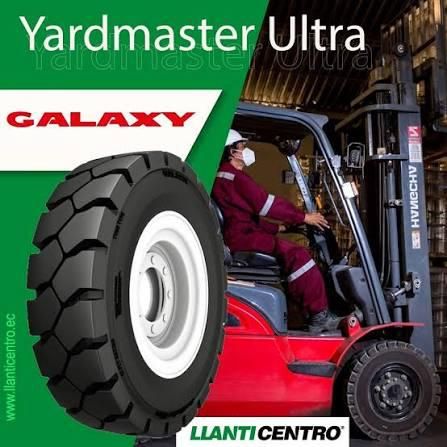 Un neumático de carretilla elevadora Galaxy Yardmaster Ultra delante de un operario que conduce una carretilla elevadora roja en un almacén.