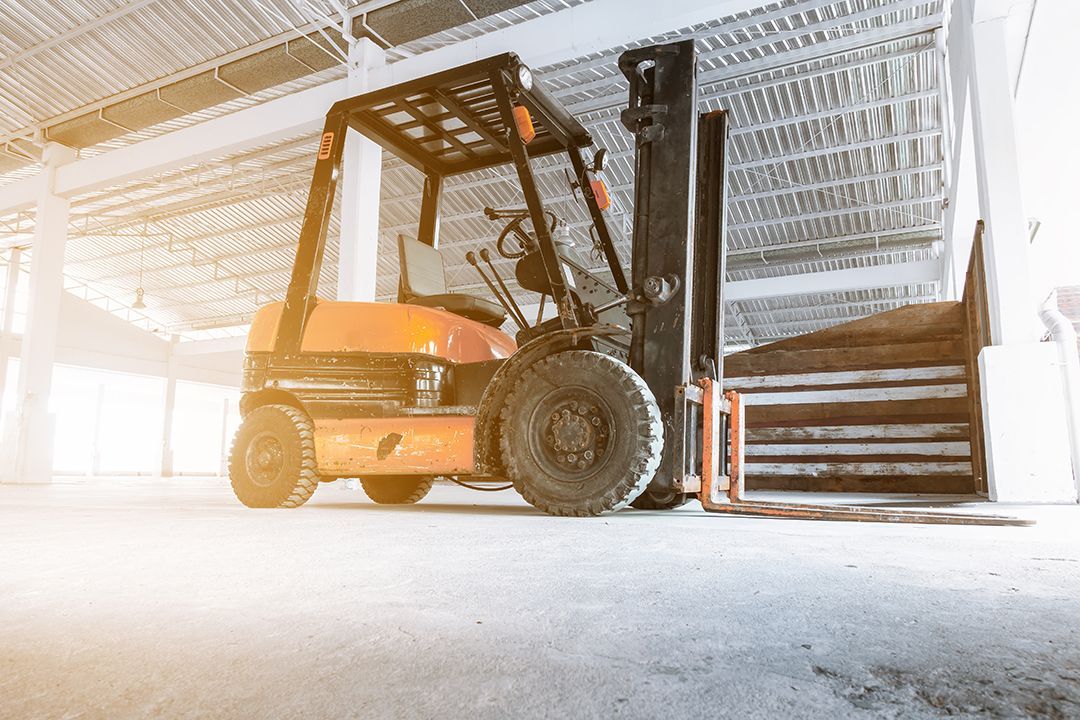 Una carretilla elevadora naranja permanece estacionada sobre un suelo de hormigón en un almacén con paredes de chapa ondulada.