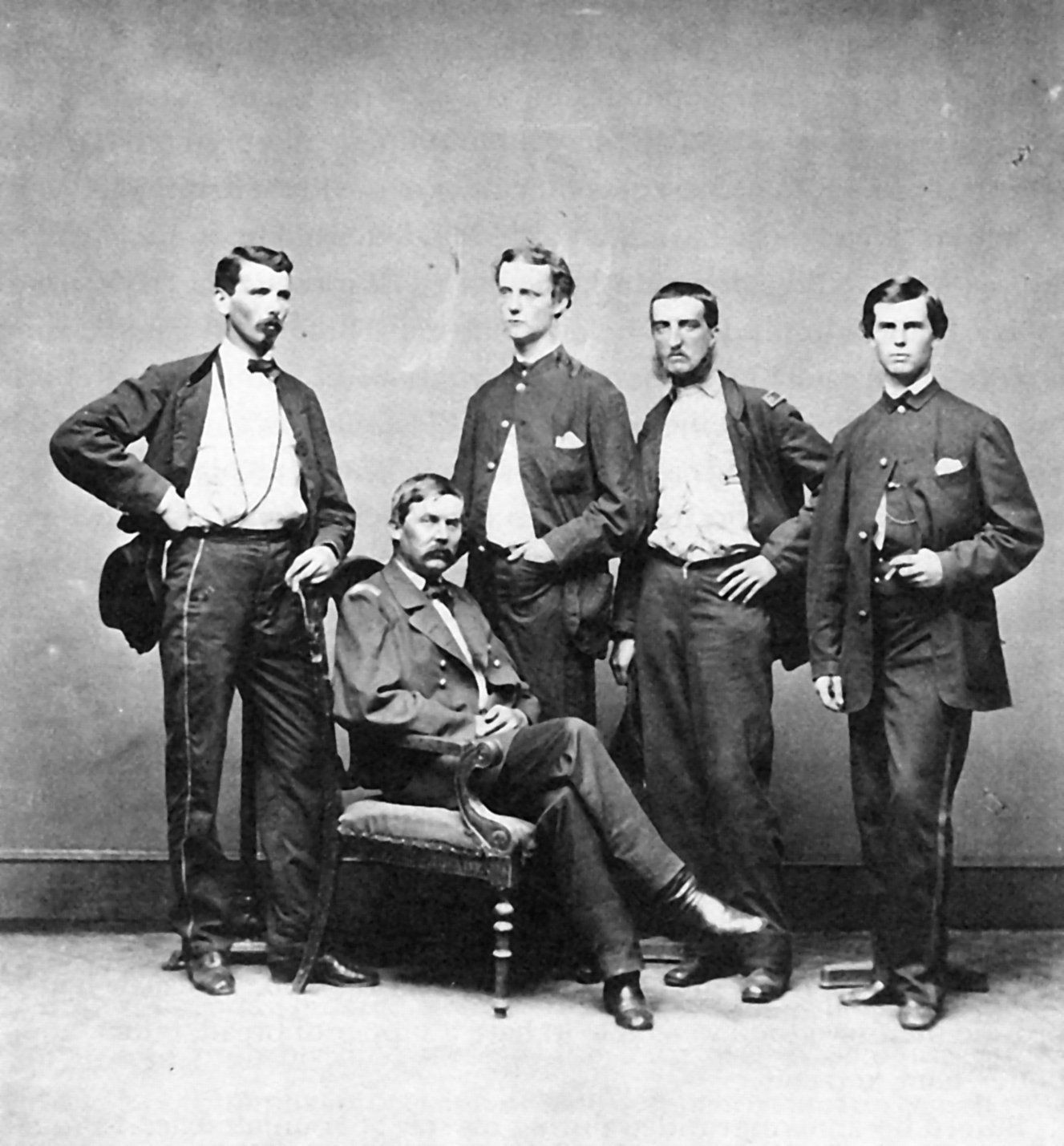 Five men in 19th-century clothing pose in a studio portrait, one seated and four standing.