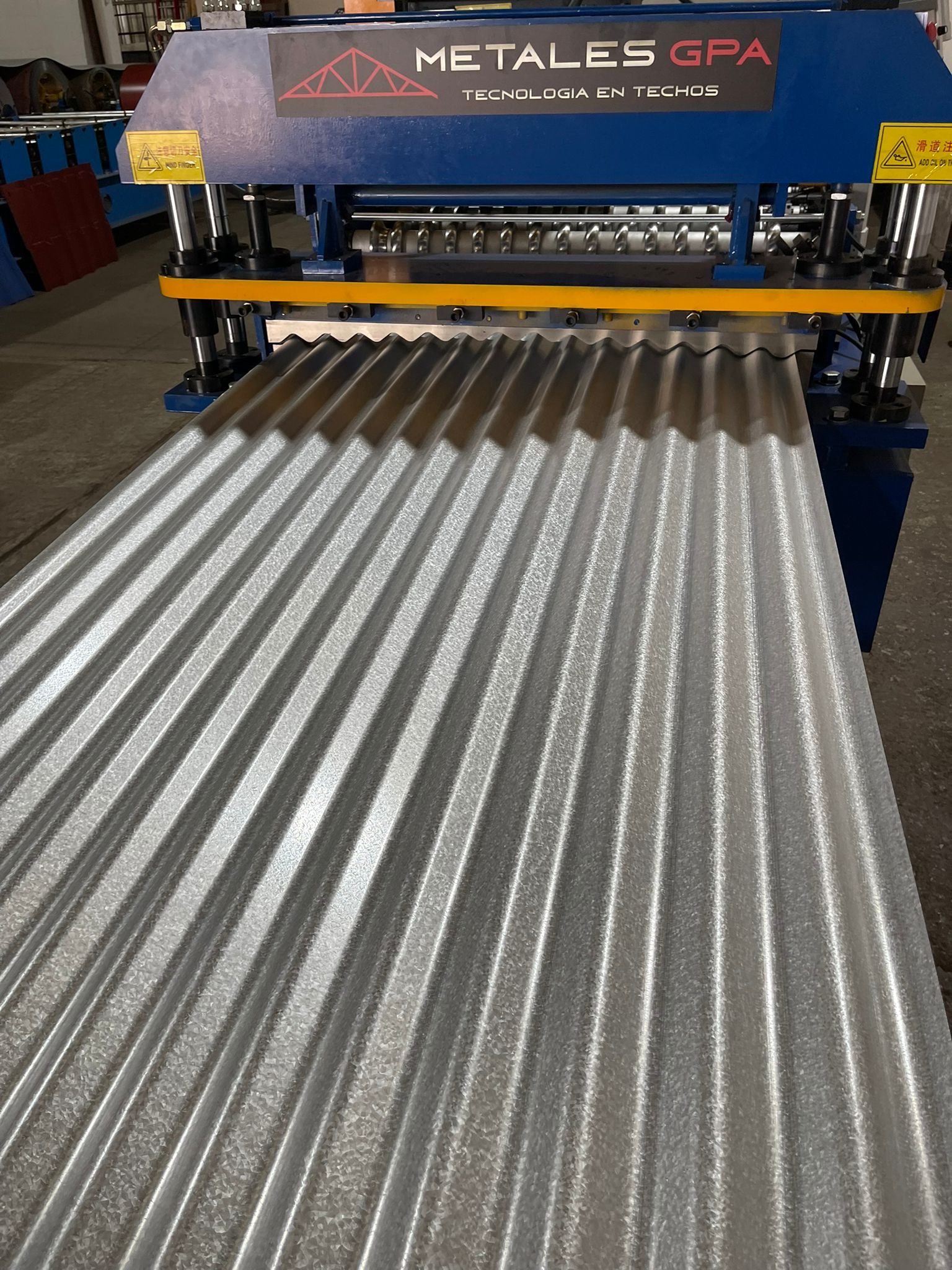 Chapa ondulada siendo formada por una máquina industrial de color azul y negro, dentro de una fábrica.