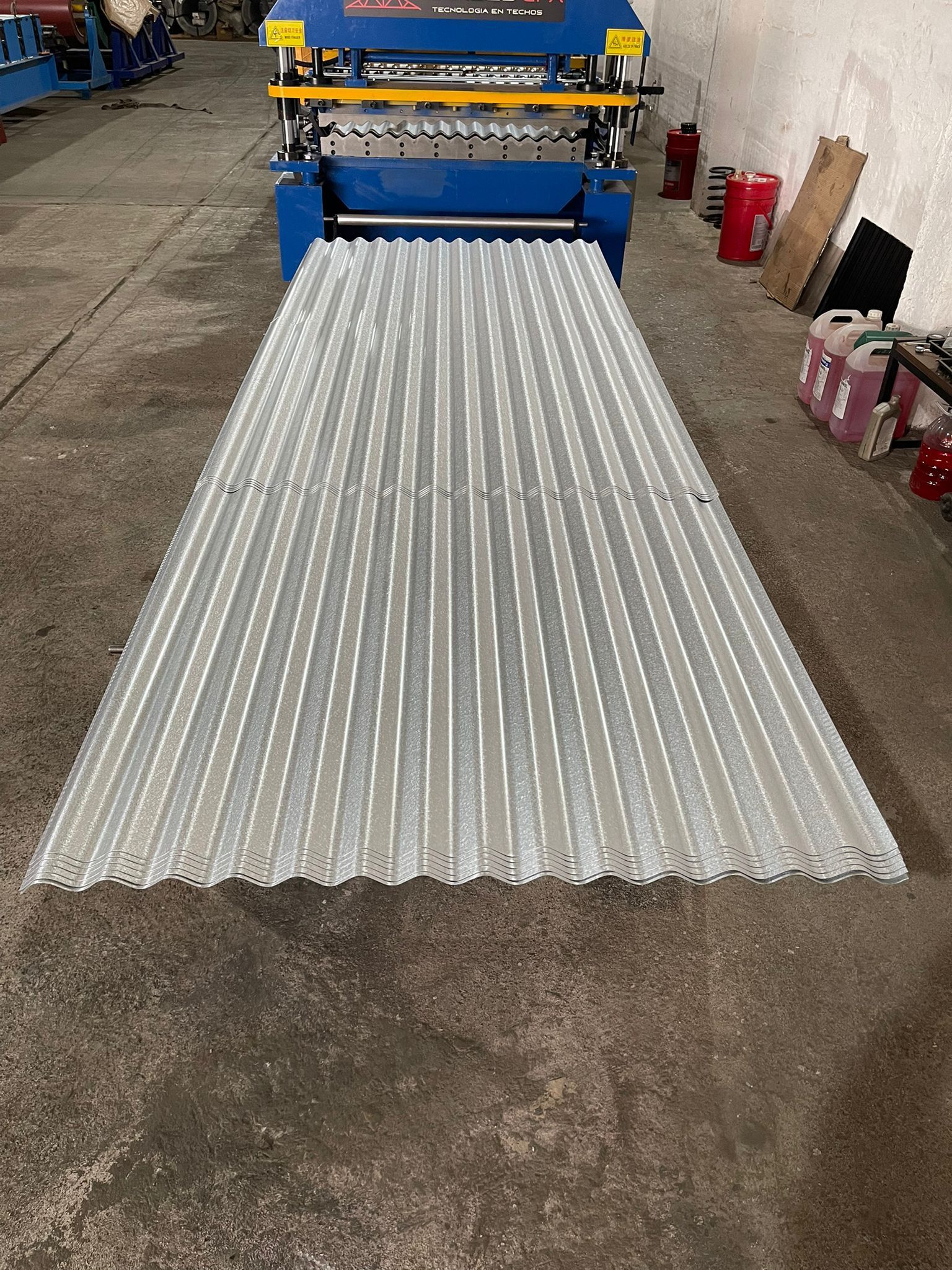 Láminas de metal corrugado que emergen de una máquina industrial azul.