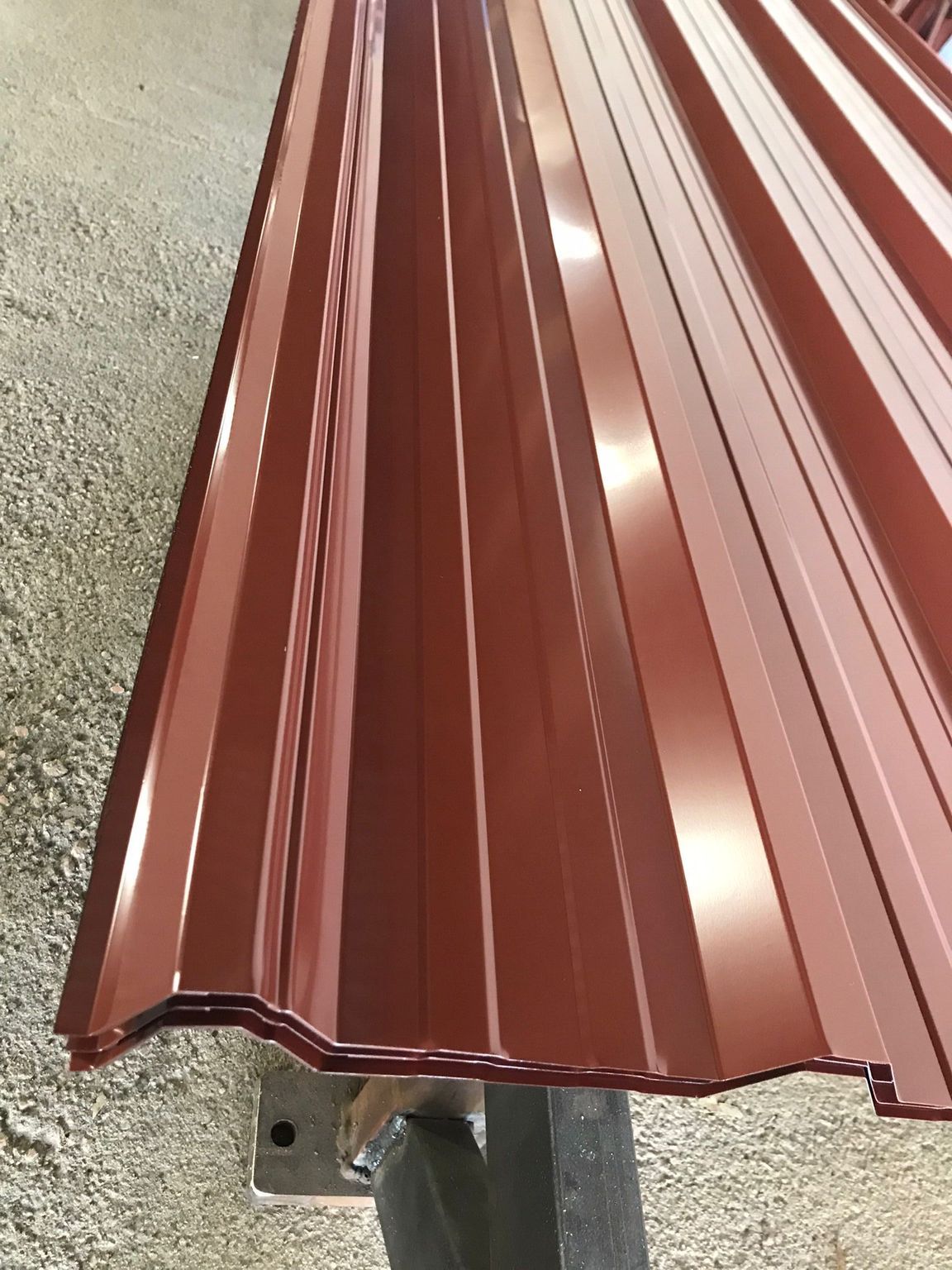 Primer plano de una lámina de metal corrugado de color granate, probablemente para techado, apoyada sobre un soporte de metal.