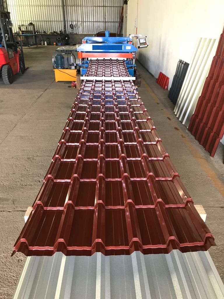 Una máquina que forma láminas metálicas marrones y largas para techos en una fábrica.