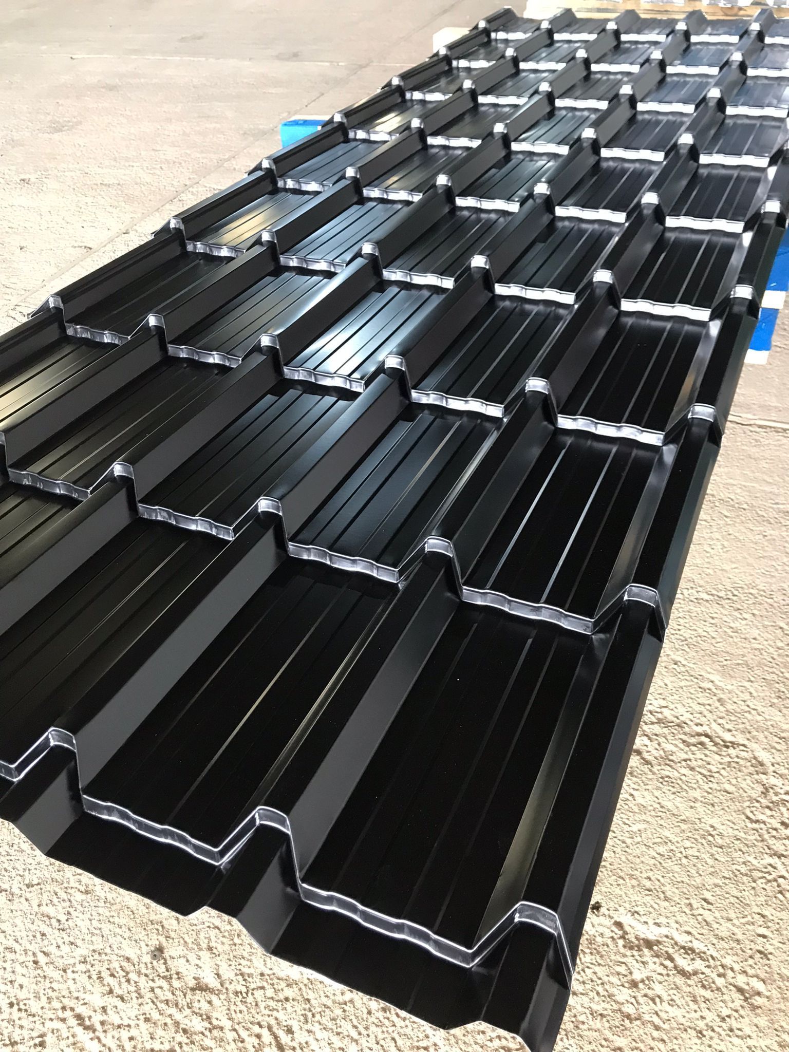 Tejas metálicas negras apiladas sobre un palé al aire libre.