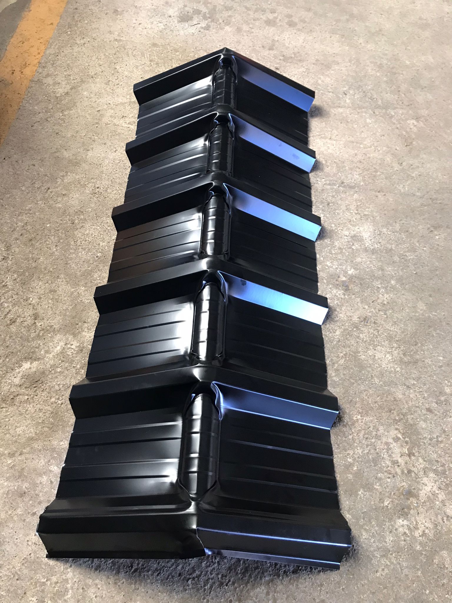 Componentes de canalón de metal negro apilados verticalmente sobre una superficie de hormigón.