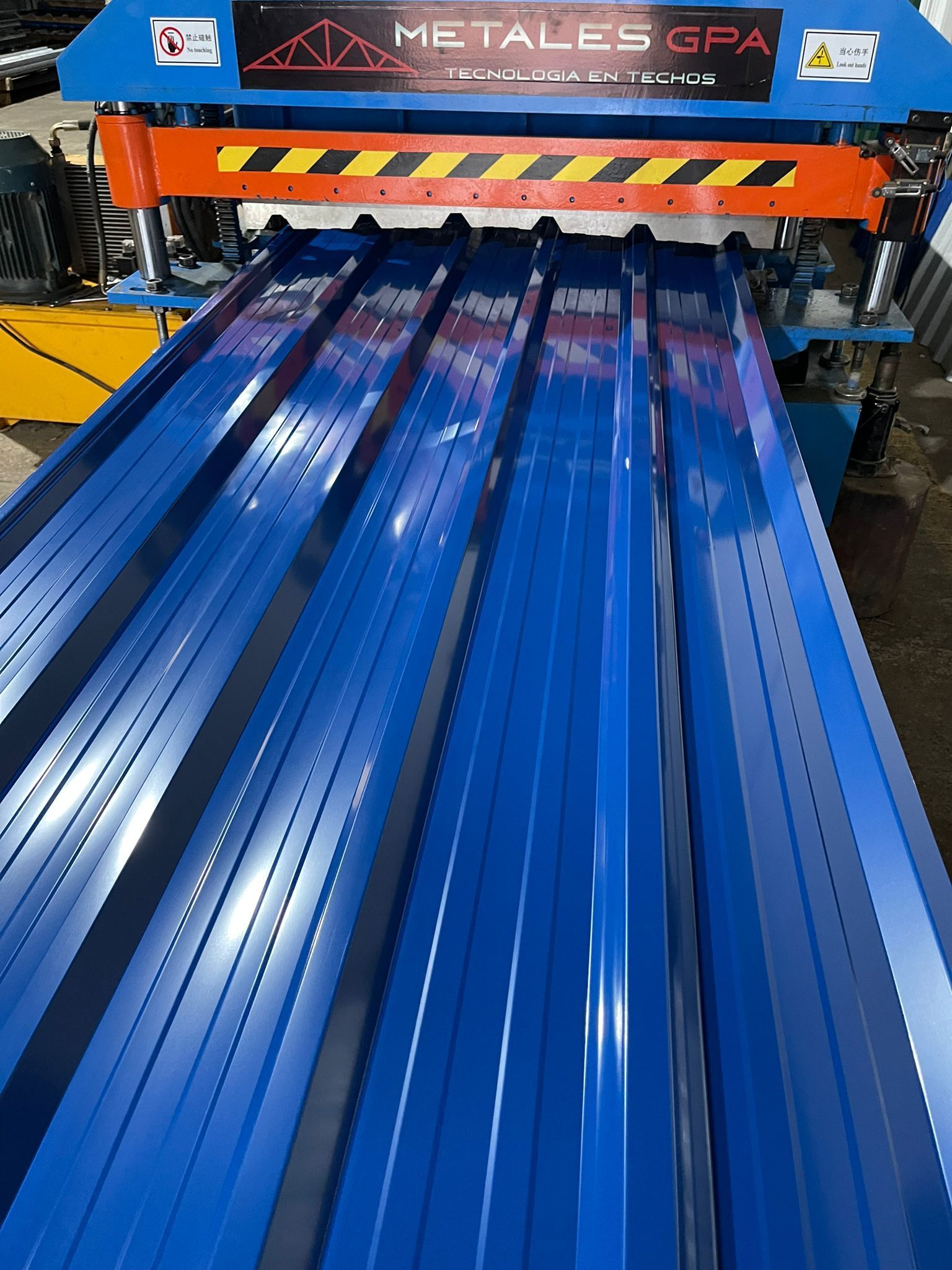 Techo de metal azul que se enrolla a través de una máquina con características de seguridad de color naranja y negro.