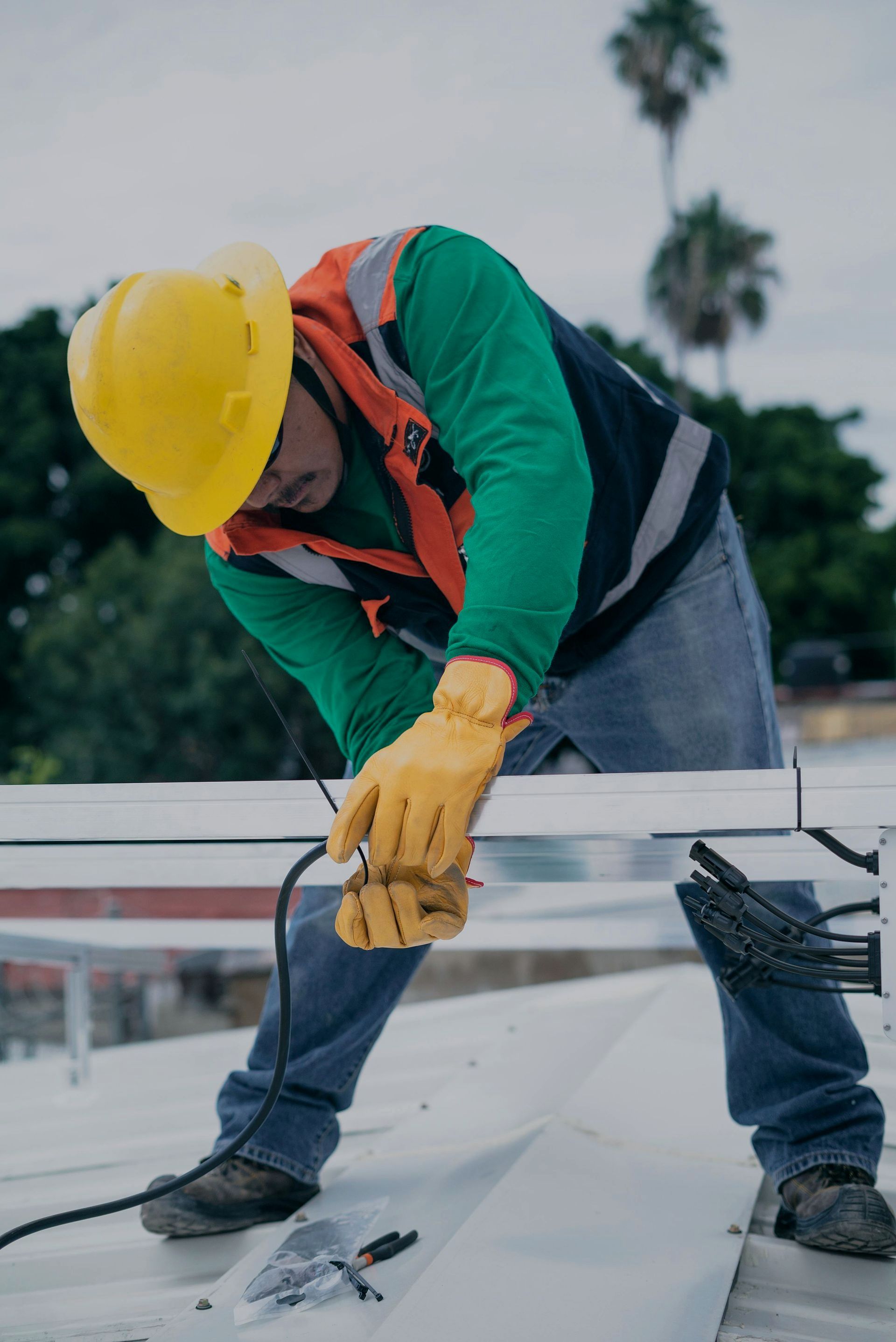 A man wearing a hard hat and gloves is working on a solar panel on a roof.