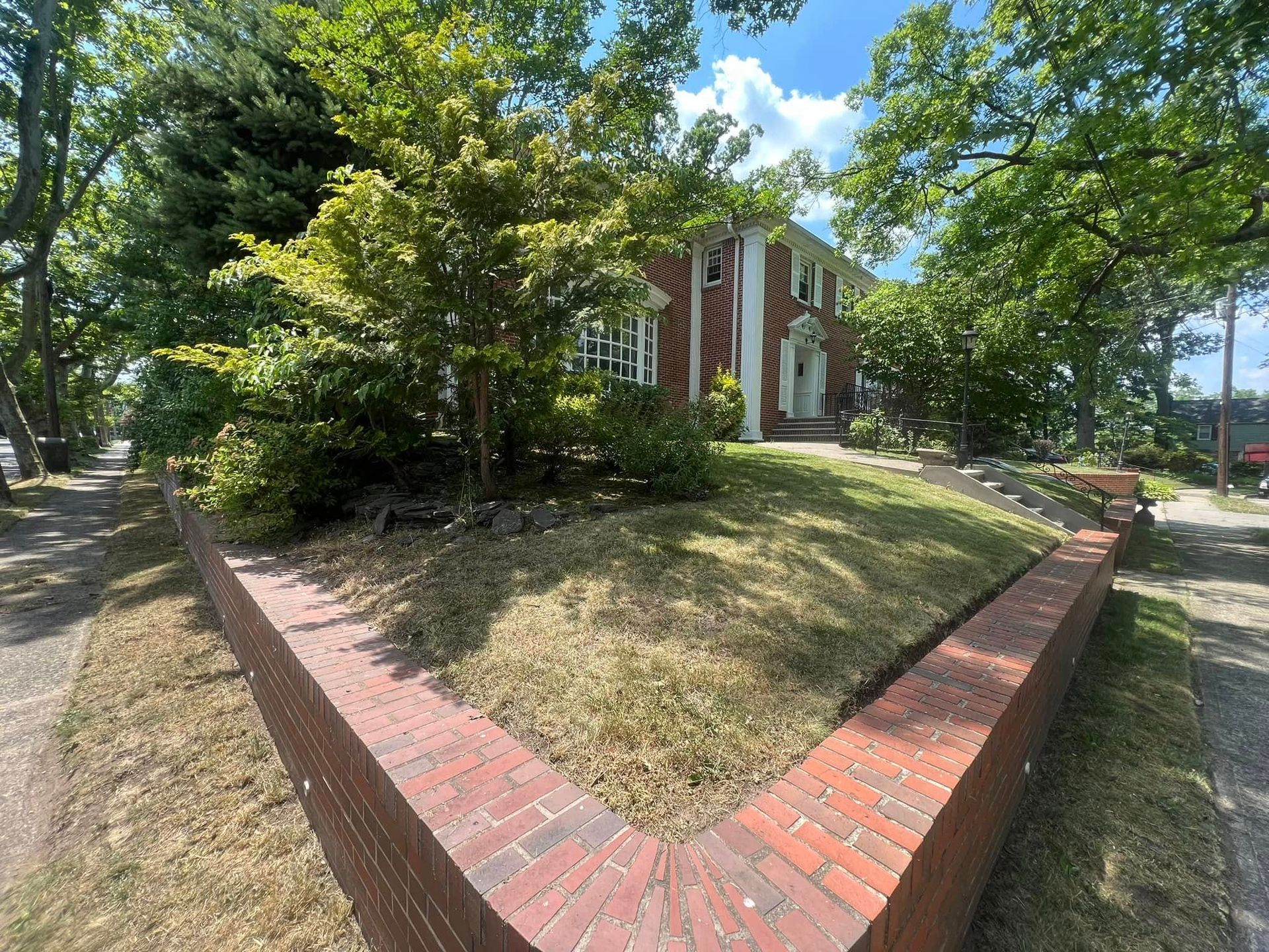 There is a brick wall in front of a house surrounded by trees.