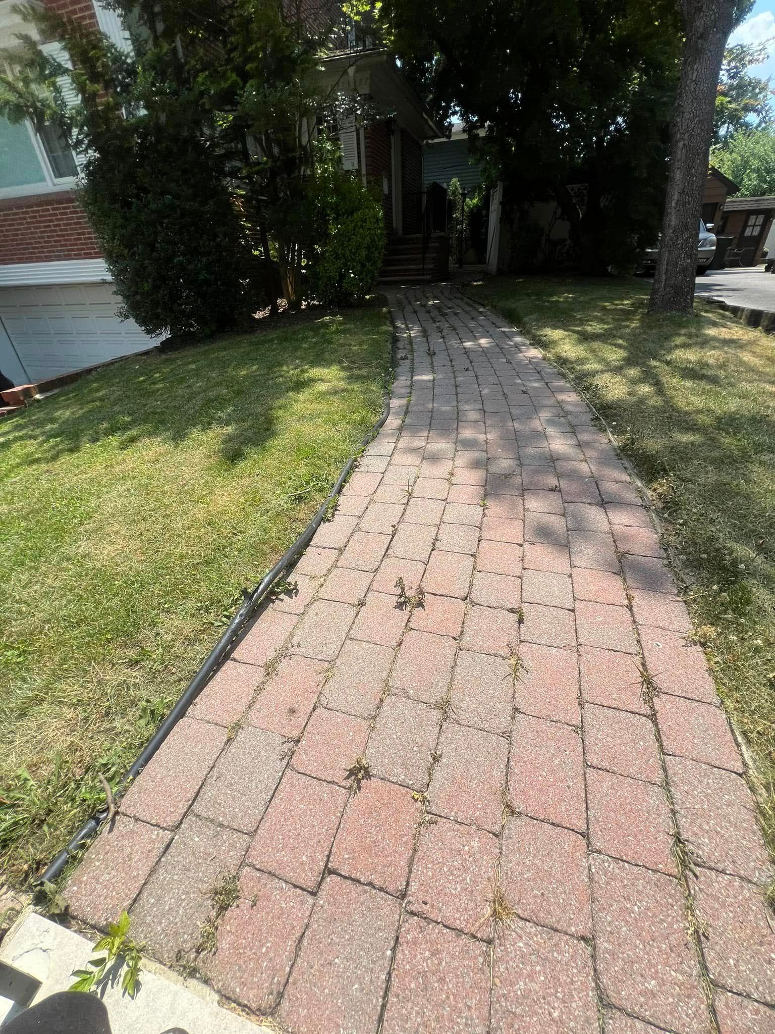 A brick walkway leading to a house with a lush green lawn.