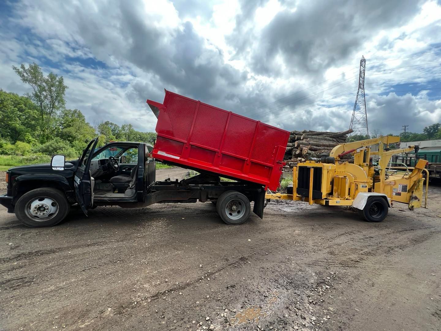 A dump truck with a red dumpster attached to it is parked next to a wood chipper.