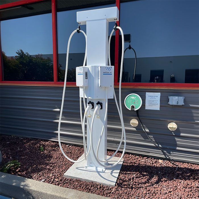 The white Wattz Up Dual Retraction Pedestal is installed in front of a commercial building and holds two white EV chargers, while cleanly keeping cables off the ground.