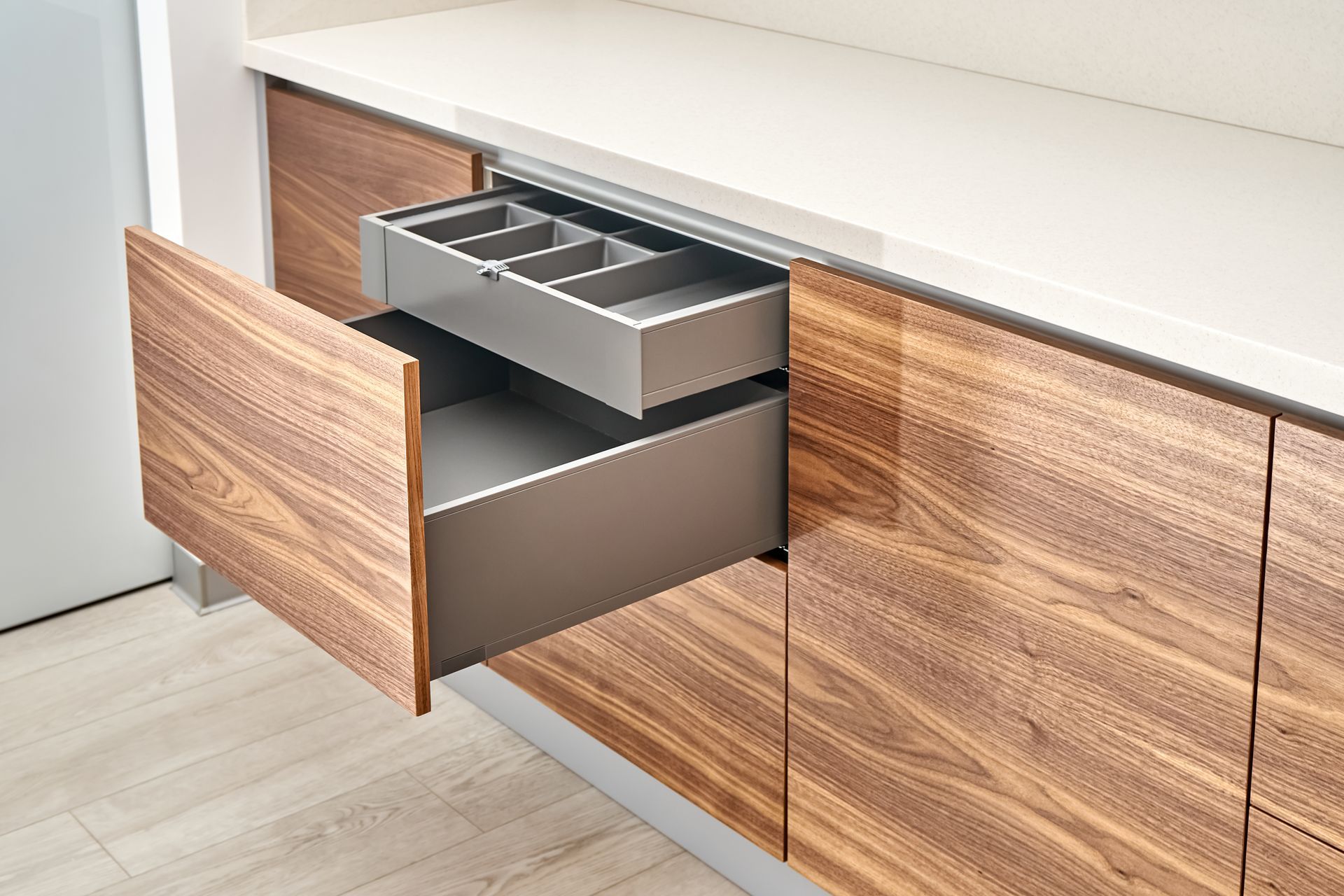 Wooden kitchen drawers, one open revealing a silverware tray.