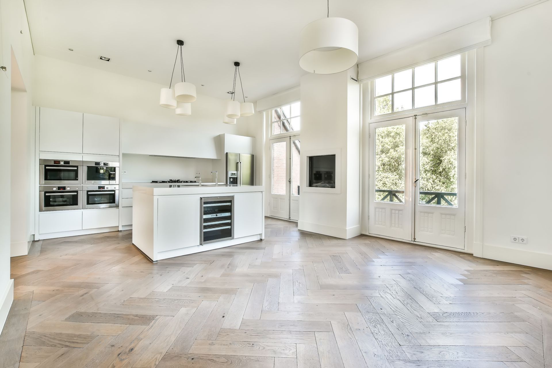 Bright white kitchen with island, light wood floor, and large windows.