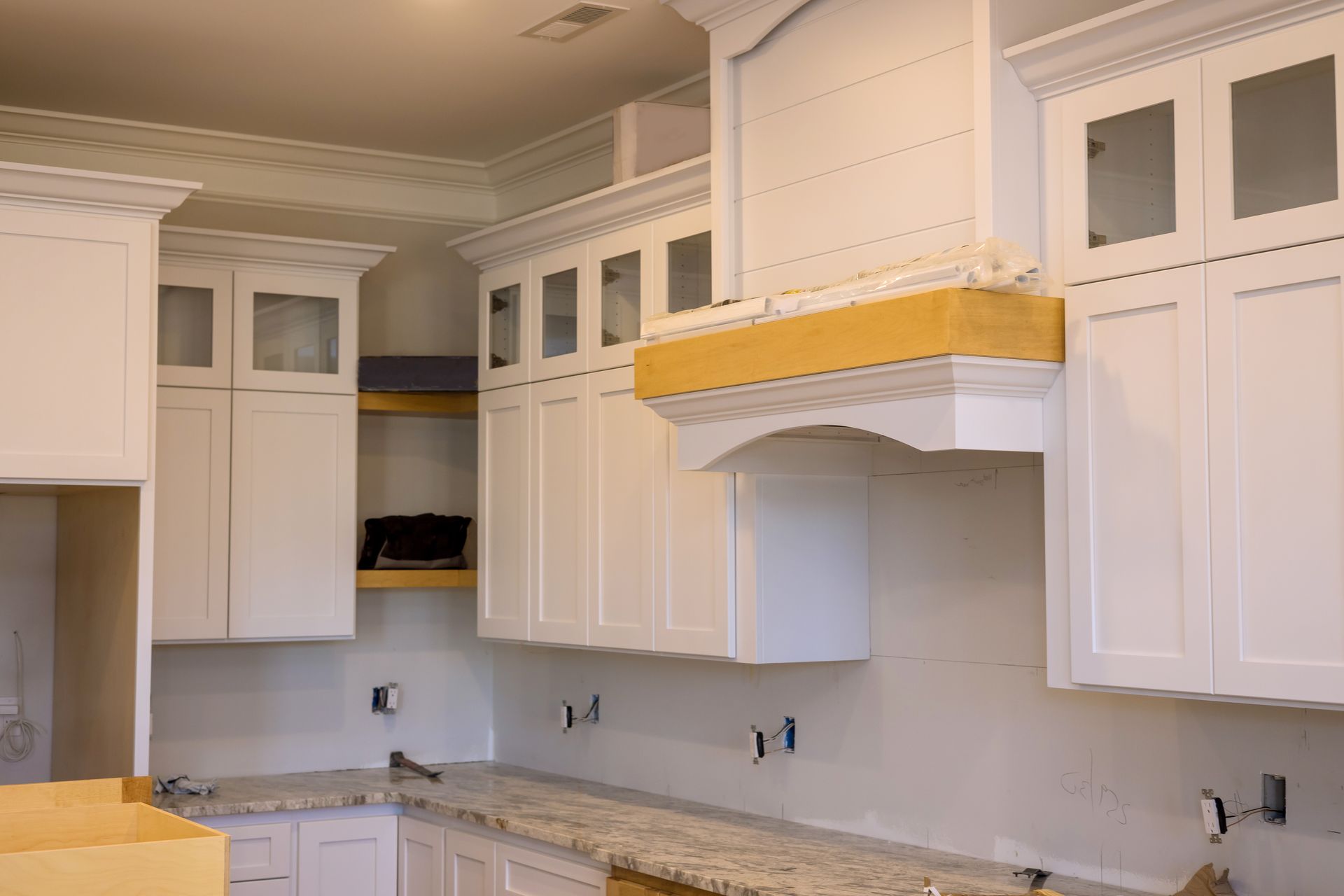 Kitchen with white cabinets, granite countertop, and a range hood under construction.
