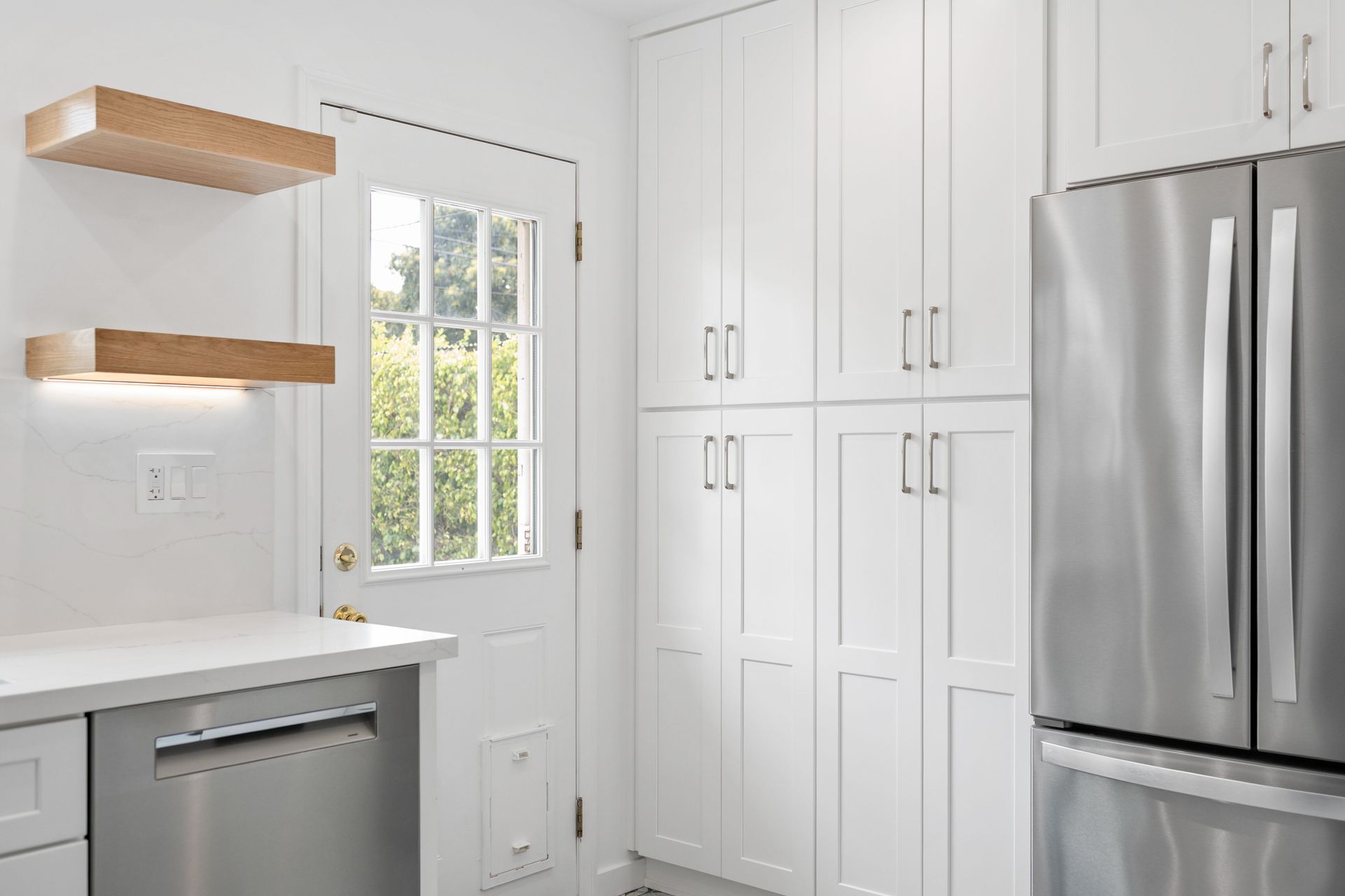 White kitchen with built-in cabinets, stainless steel refrigerator, and floating wooden shelves.