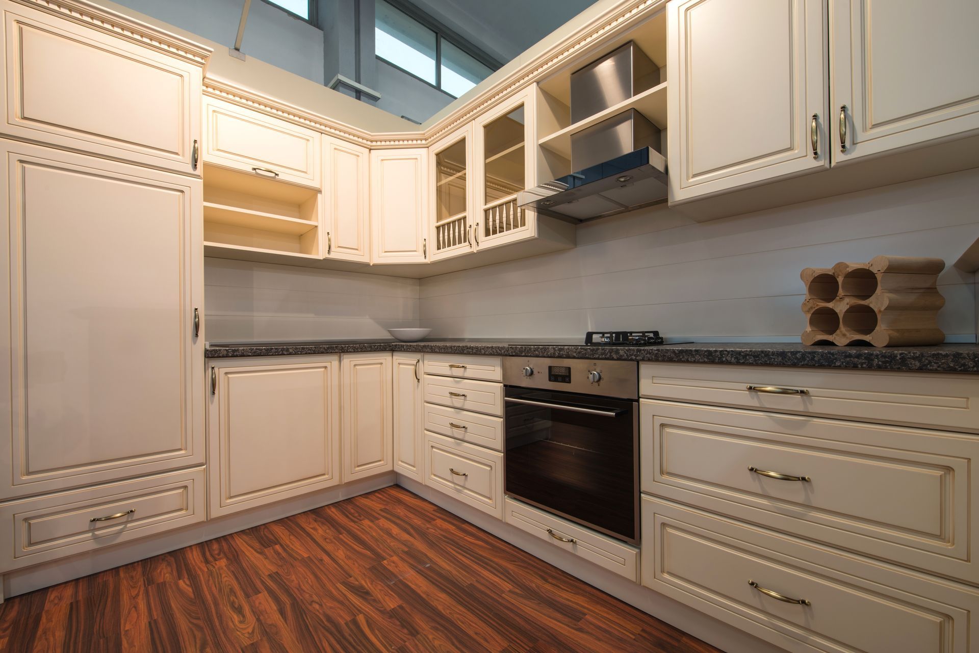 Cream-colored kitchen cabinets with granite countertops, built-in oven, and dark wooden flooring.