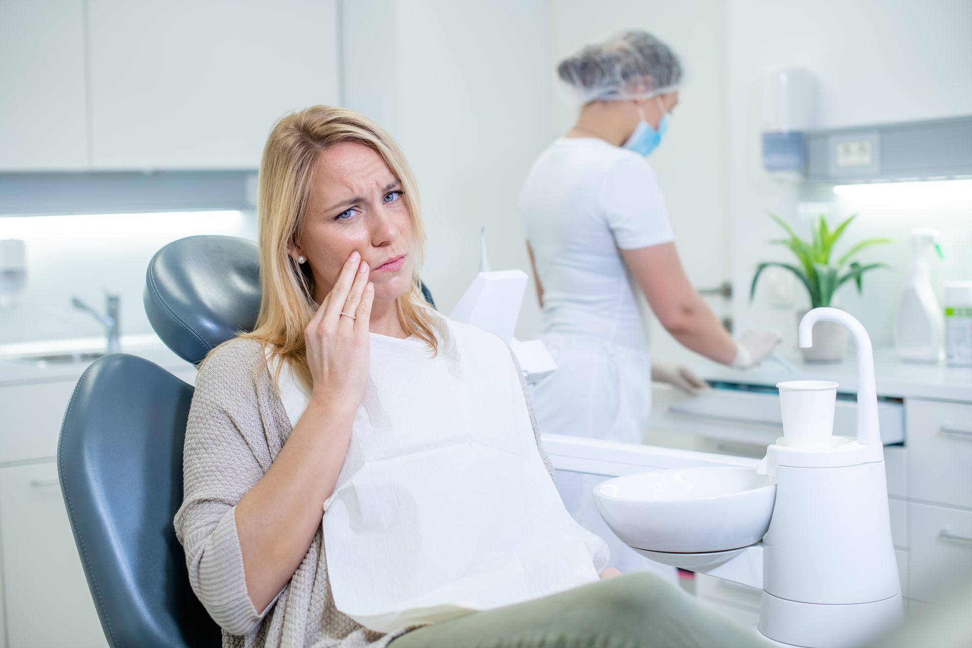 A woman suffering from a toothache at a dental clinic. A dentist is preparing for examination.