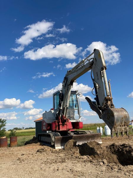 A red and white excavator is digging a hole in the dirt.