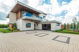 A large modern house with a brick driveway in front of it.