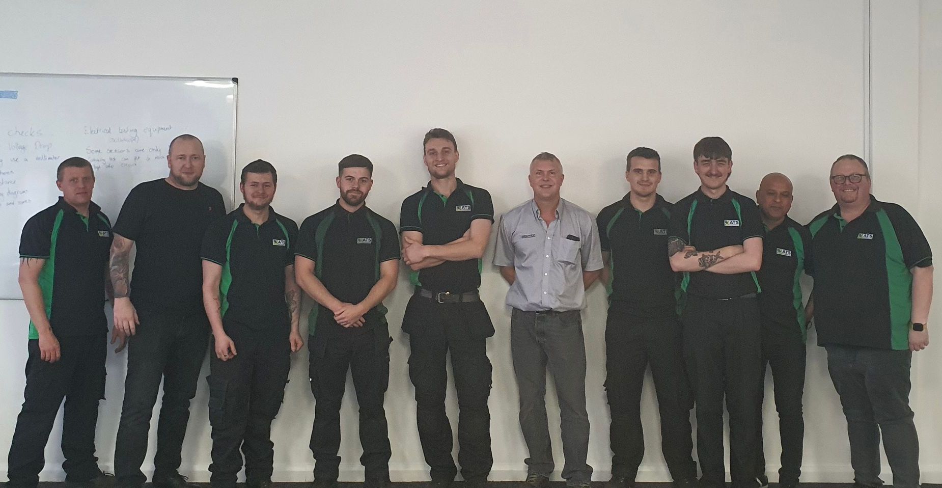 A group of men are posing for a picture in front of a white board.