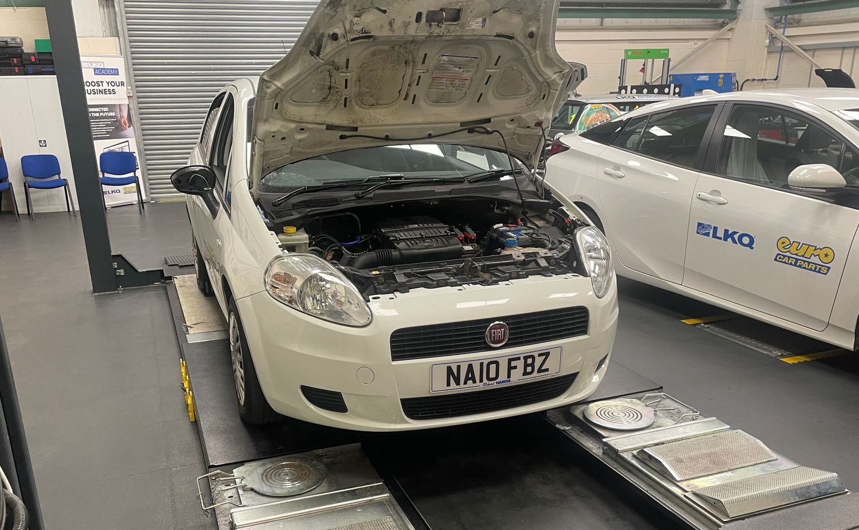 A white car with the hood up is sitting on a lift in a garage.