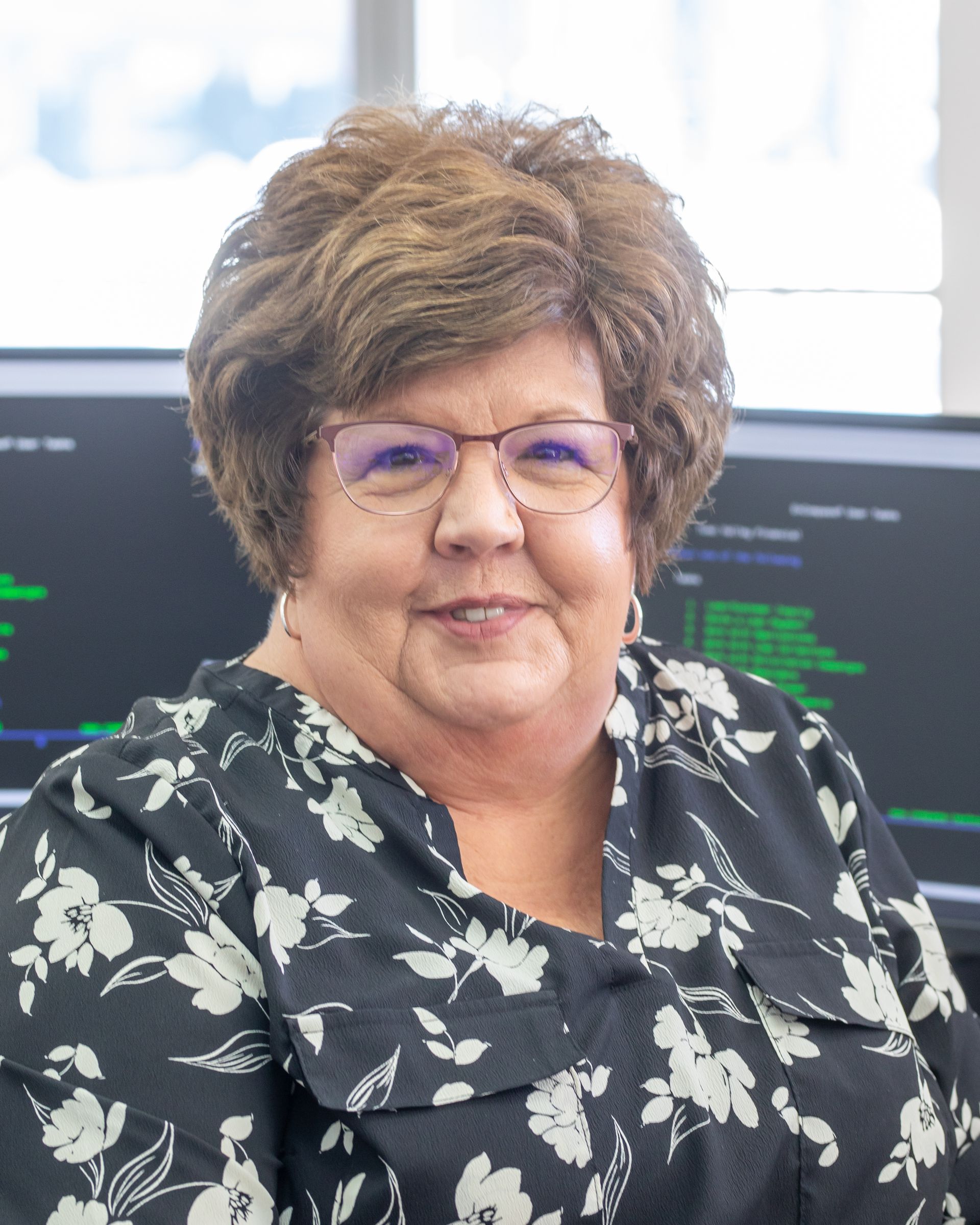 Woman with glasses smiles at the camera, wearing a black floral print blouse.