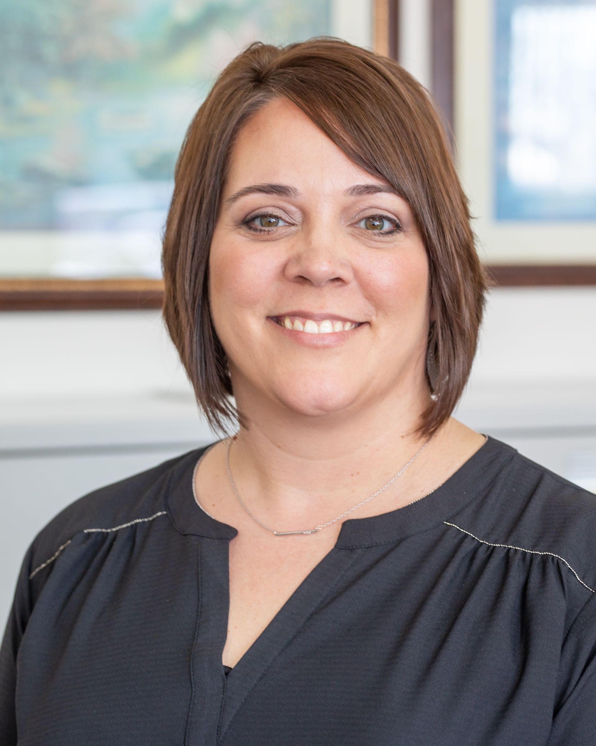 Woman with brown hair, smiling, wearing a black top, in an office setting.