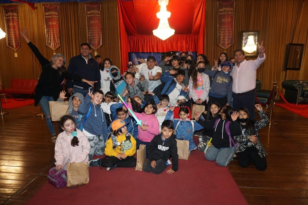 Grupo de niños y adultos posando en una habitación adornada con alfombra roja y lámpara de araña.