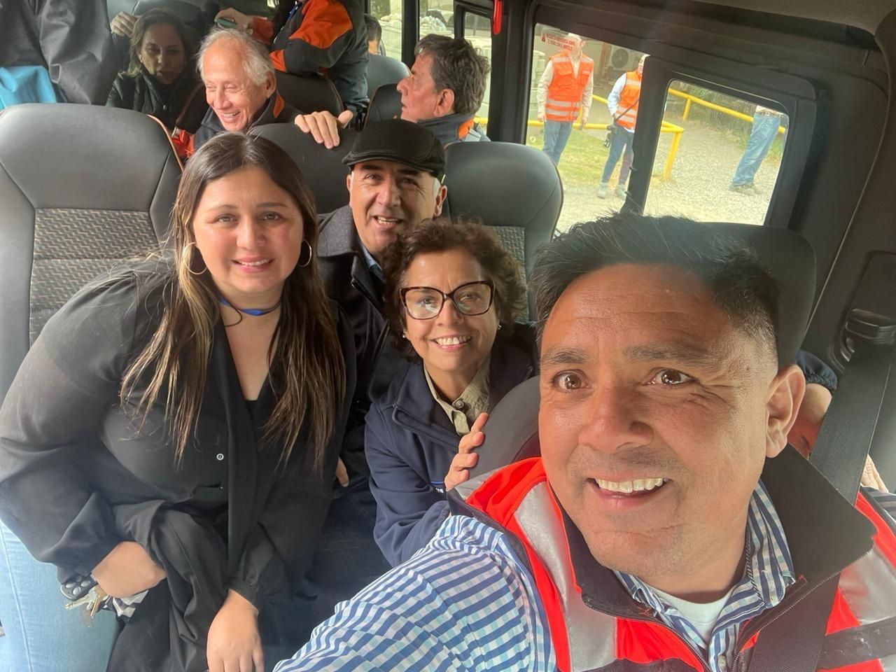 Gente sonriendo y posando dentro de una furgoneta. Un hombre se toma una selfi. Otros llevan chaquetas y parecen felices.