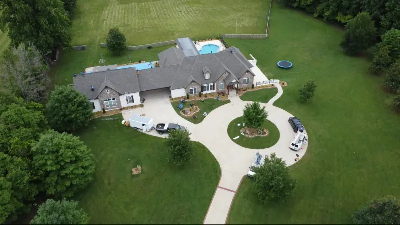 An aerial view of a large house with a pool in the backyard surrounded by trees.