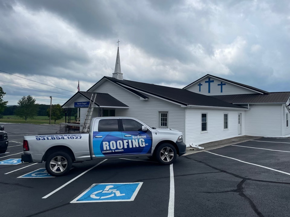 A roofing truck is parked in front of a church.