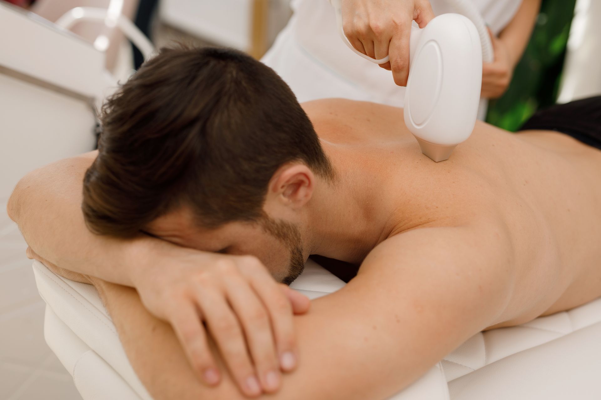 Man receiving laser hair removal treatment on his back in a medical setting.