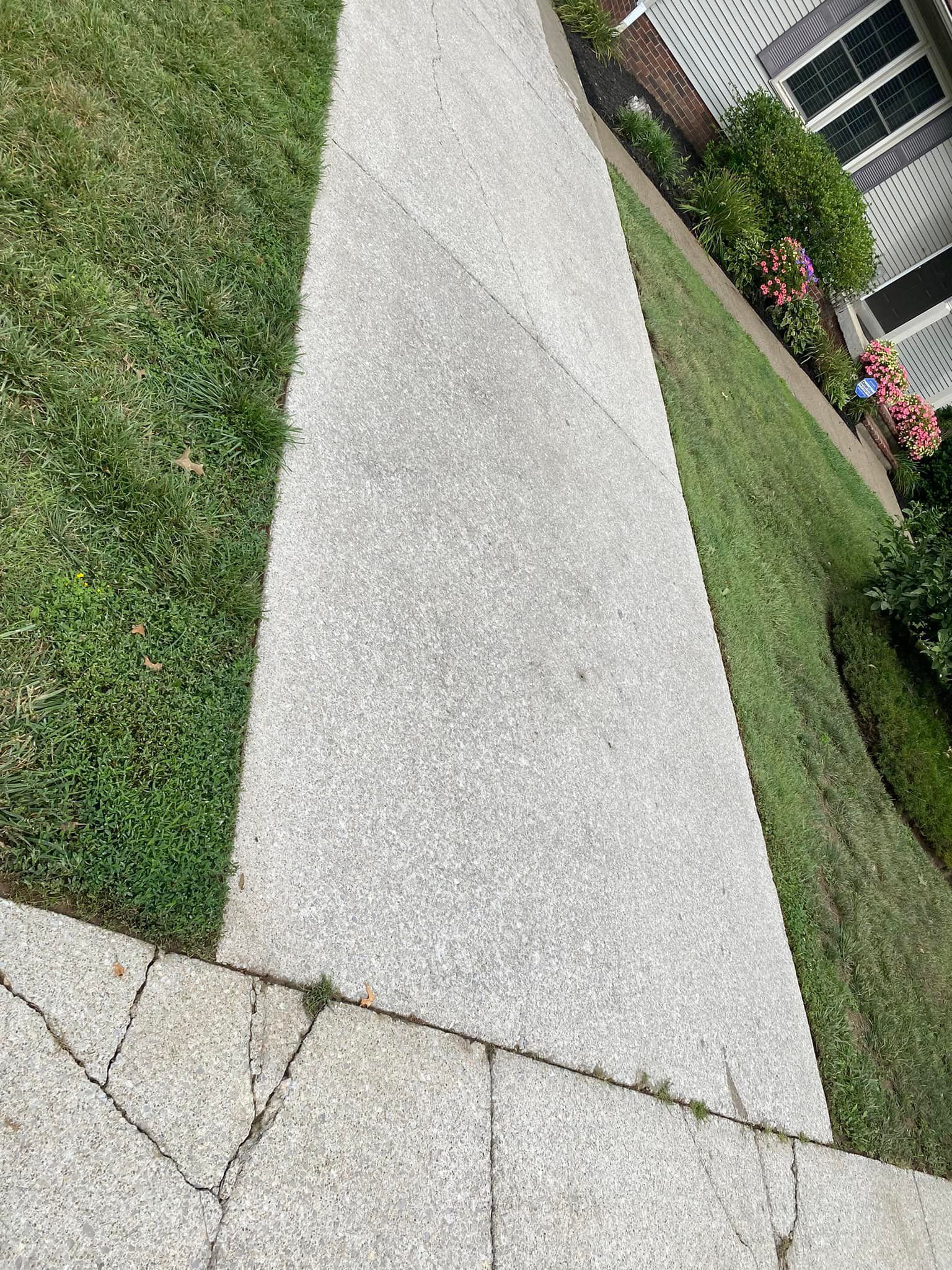 A sidewalk next to a lush green lawn in front of a house.